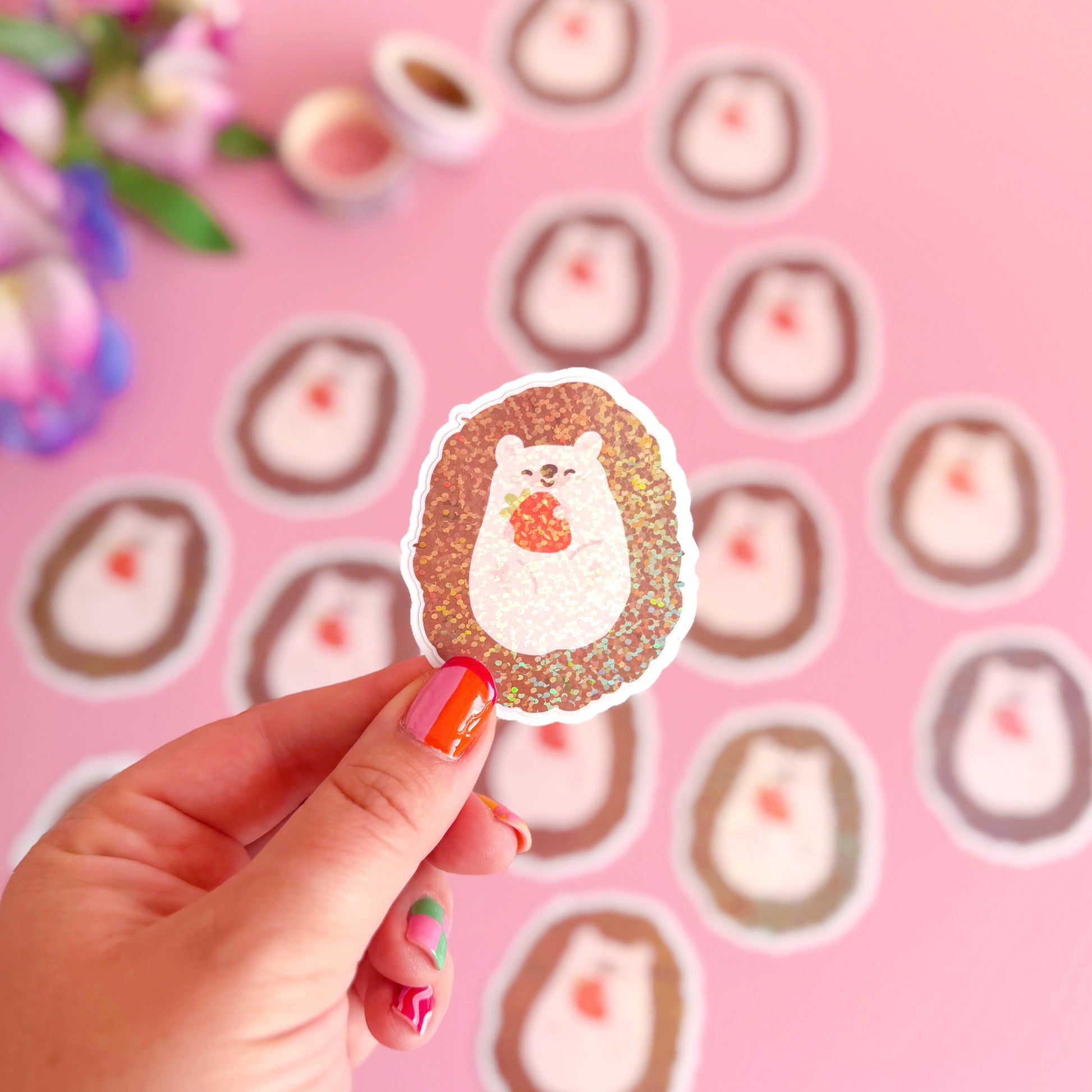 A glittery sticker of a small cute hedgehog holding a little strawberry in her hands.