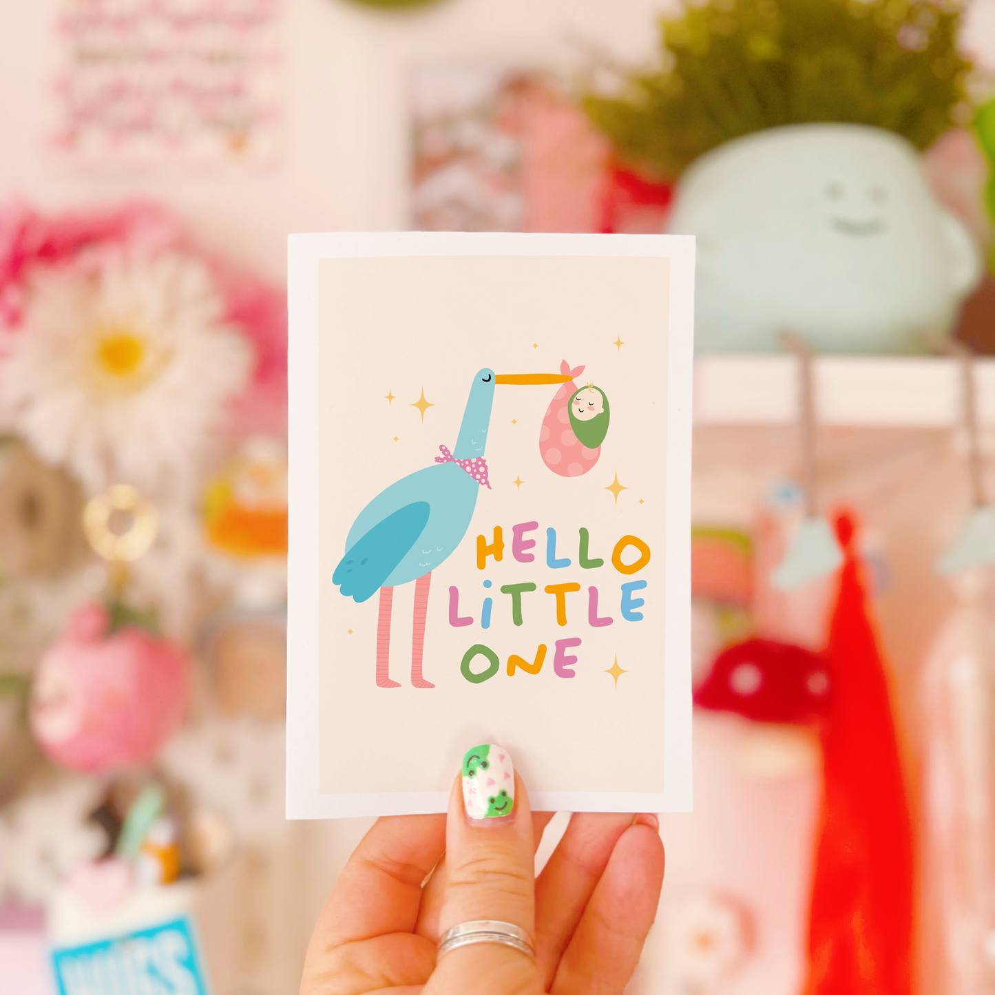 A greetings card with an illustration of a stalk carrying a baby, with the words 'hello little one' in colourful tones.