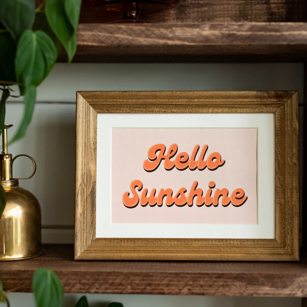 A cute quote print, with orange text saying 'Hello Sunshine' on a pale pink background.
