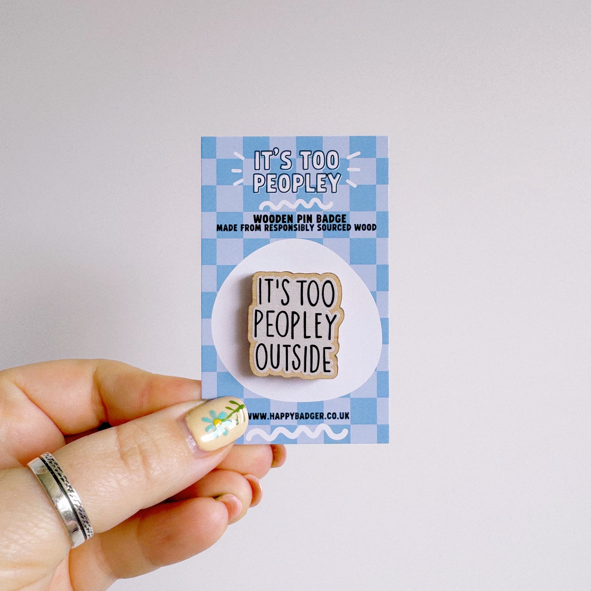 A wooden pin badge, that reads 'it's too peopley outside' on the front.