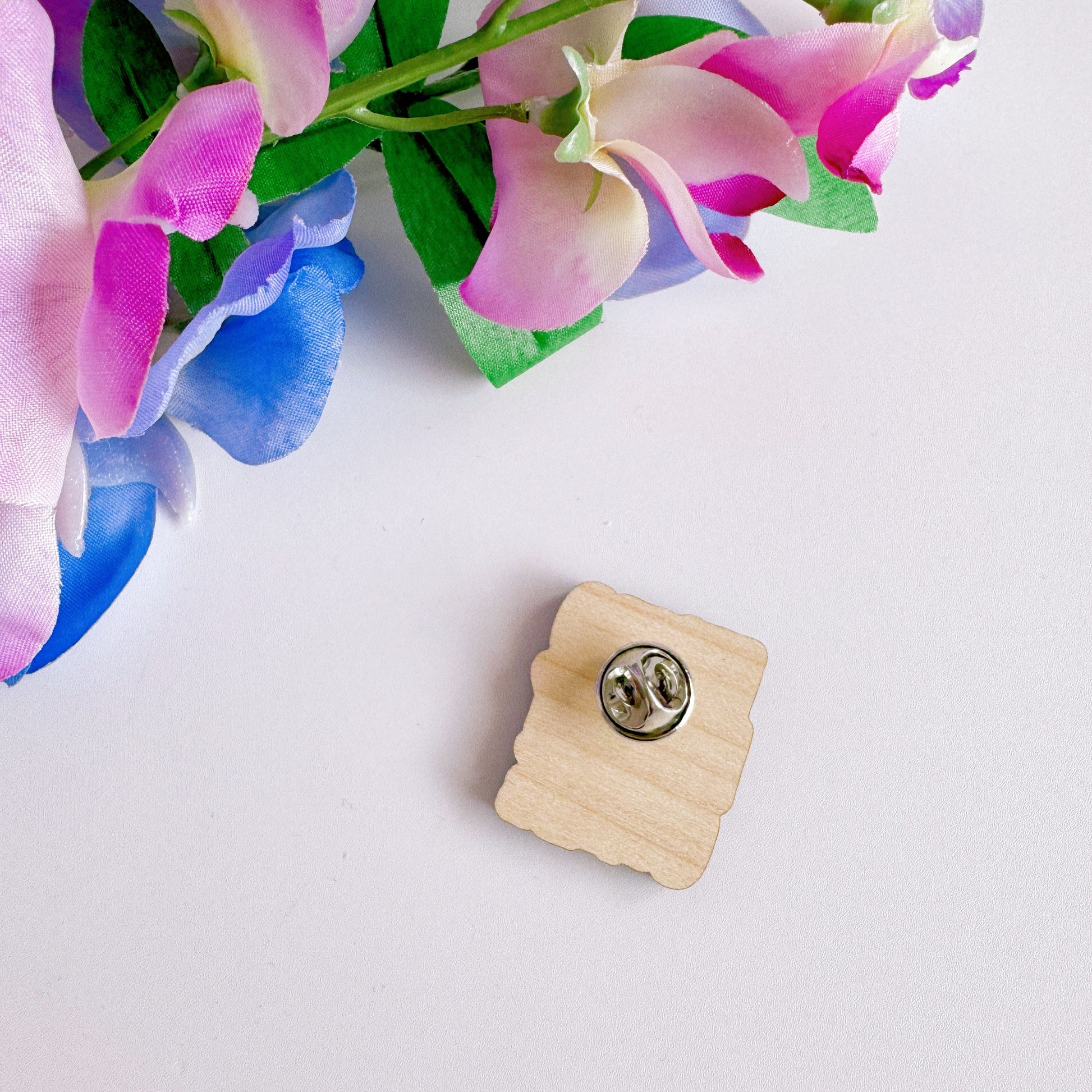 A wooden pin badge, that reads 'it's too peopley outside' on the front.