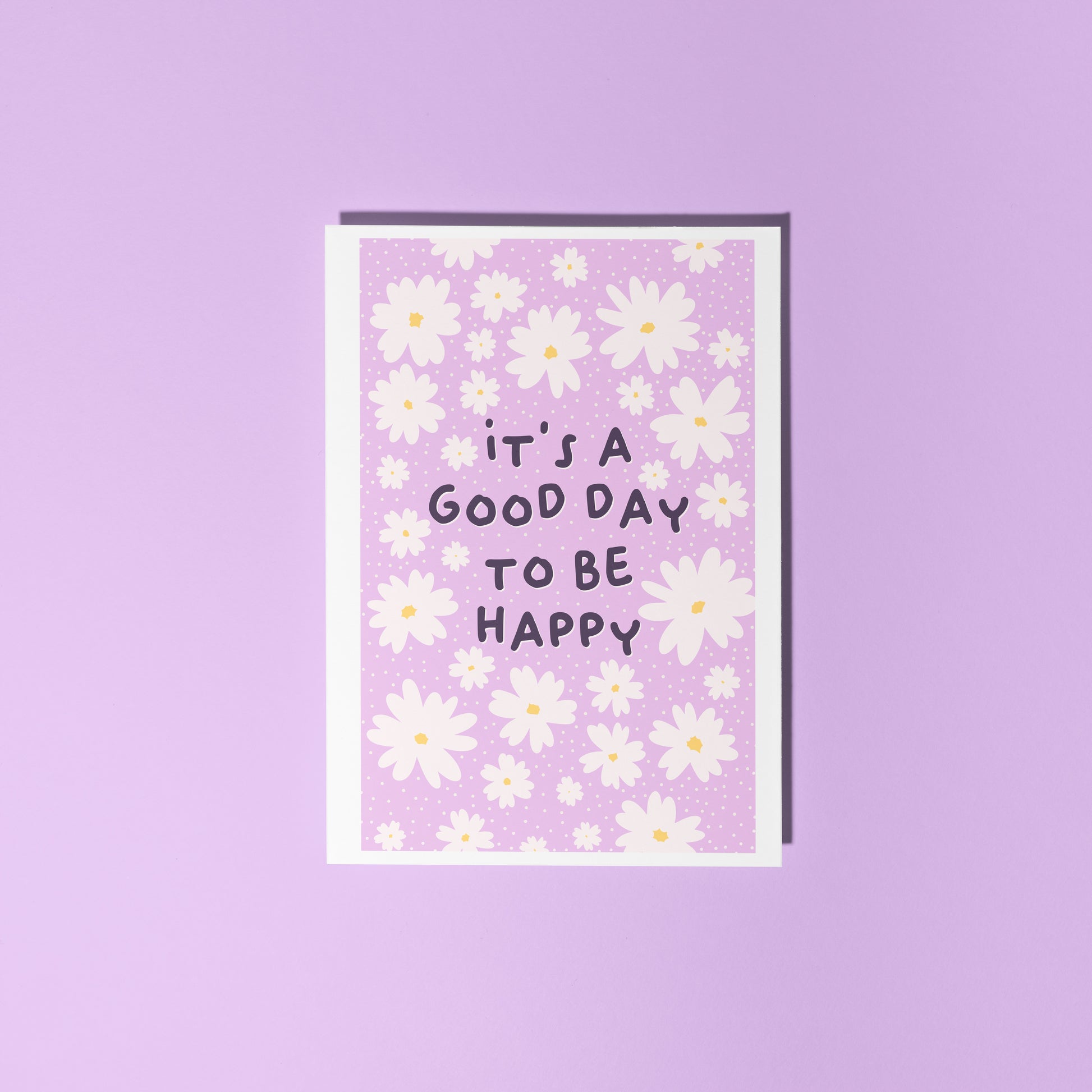 A purple card, with a white daisy pattern all over and the words 'it's a good day to be happy' in the centre.