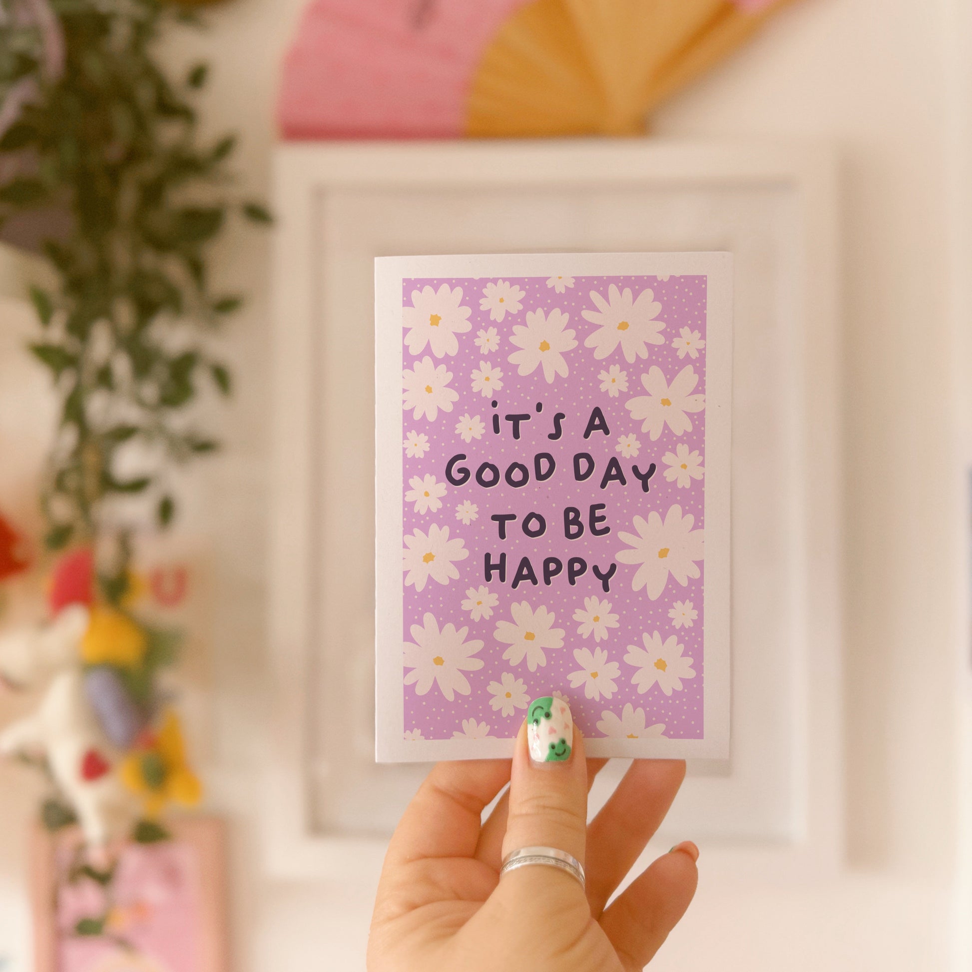 A purple card, with a white daisy pattern all over and the words 'it's a good day to be happy' in the centre.