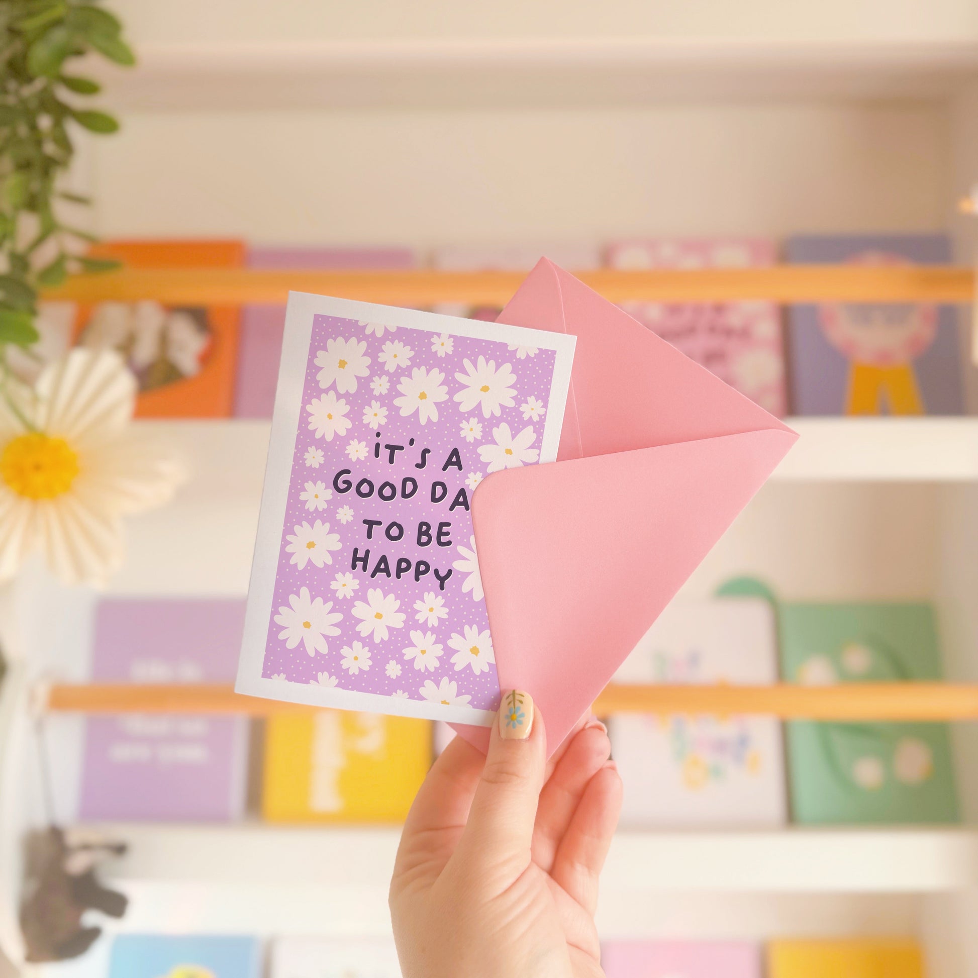 A purple card, with a white daisy pattern all over and the words 'it's a good day to be happy' in the centre.