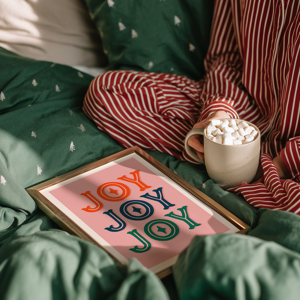 A print with a warm pink background and the word 'joy' written, in an ornate text, three times - one in red, one in navy and one in green.