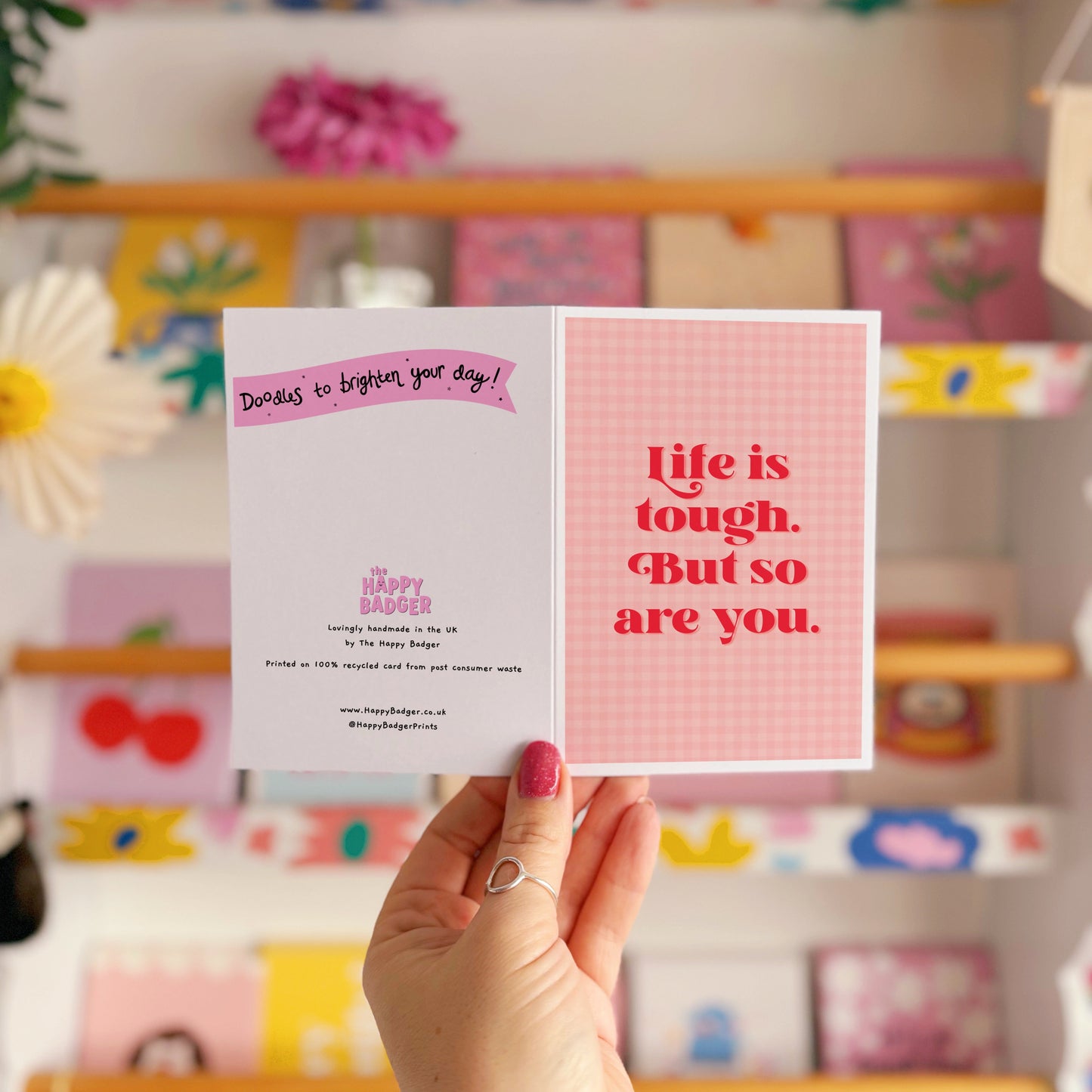 A pink and red card, that says 'life is tough but so are you.' on the front.