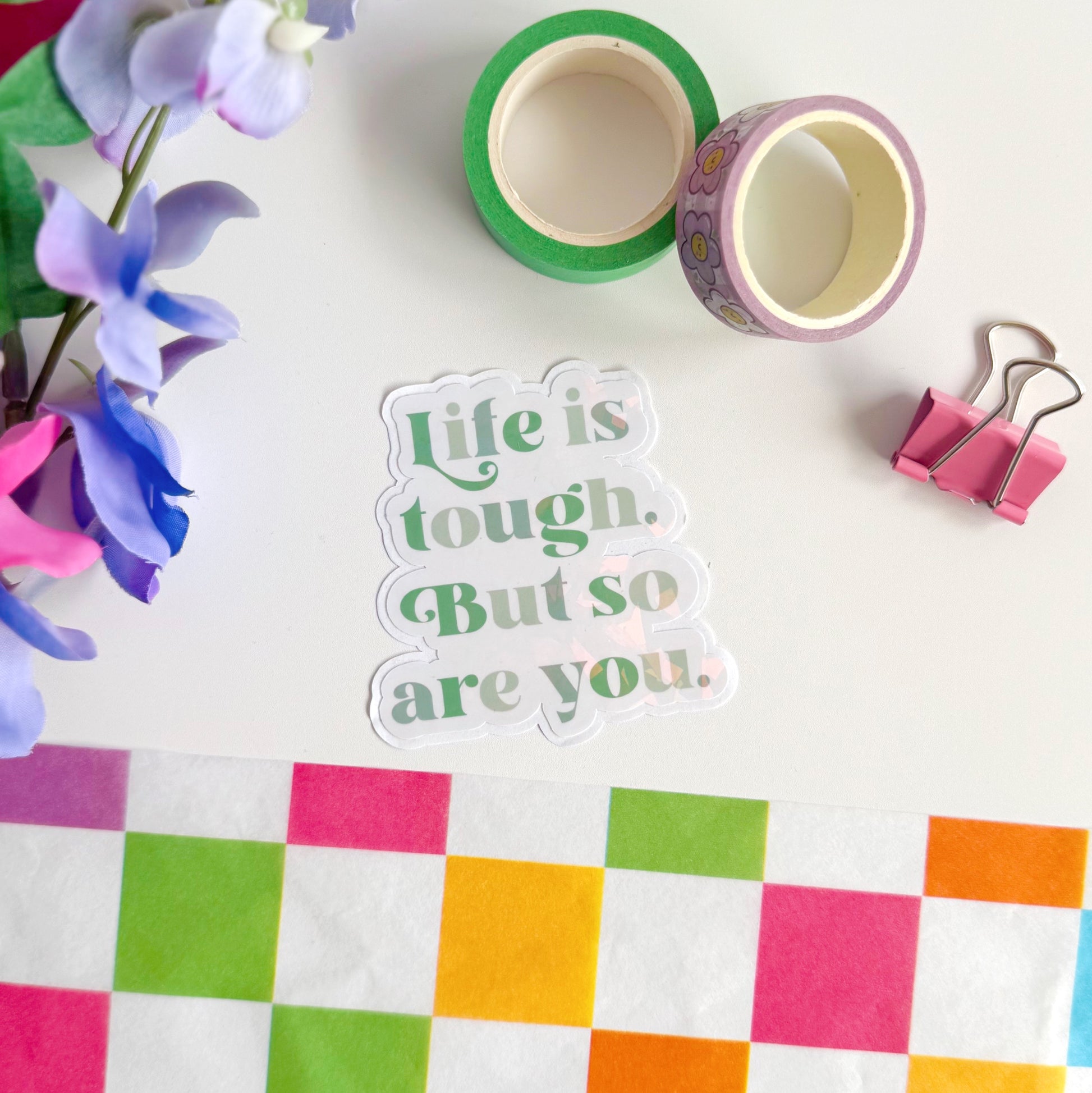 A green holographic finish sticker, with green text saying 'life is tough but so are you'.