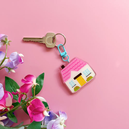 Key with a colorful house-shaped keychain on a pink background with flowers.