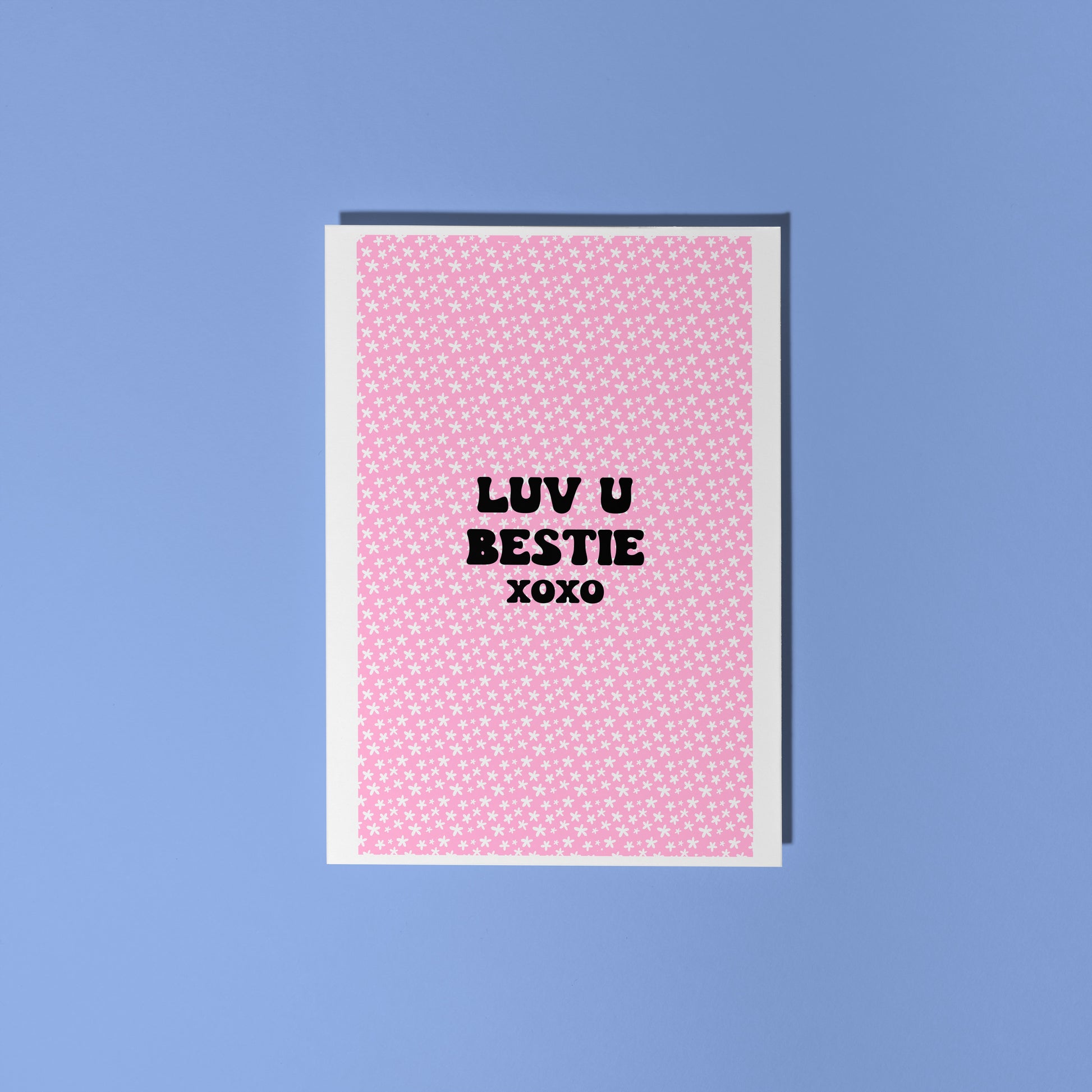 A pink greetings card, with a pink floral pattern, and text in black saying 'Luv U Bestie xoxo' in the centre front.