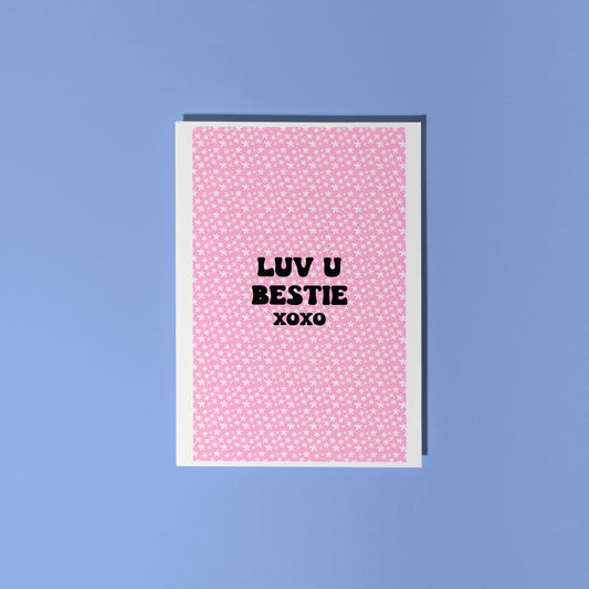 A pink greetings card, with a pink floral pattern, and text in black saying 'Luv U Bestie xoxo' in the centre front.