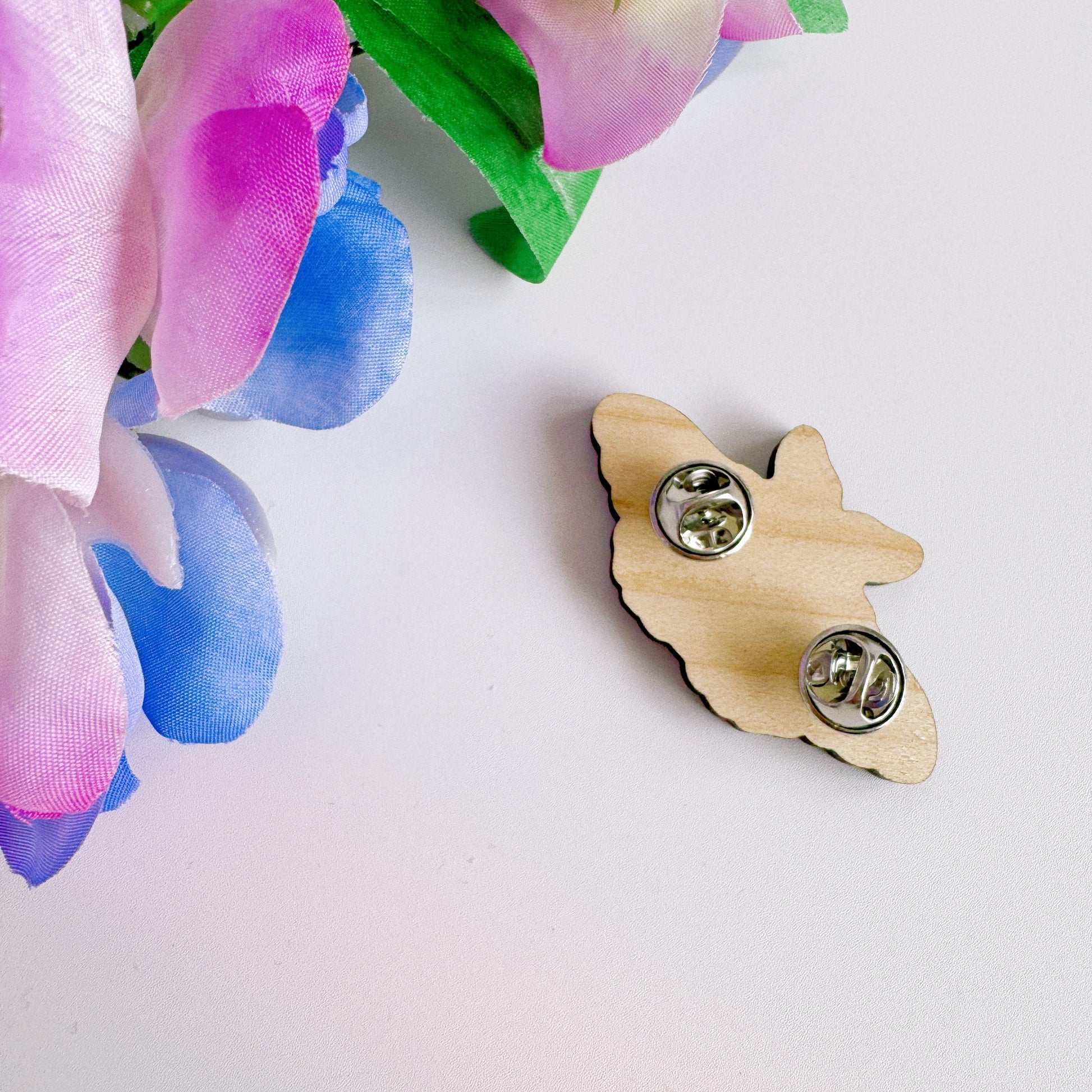 A wooden pin badge of a purple and pink moth.
