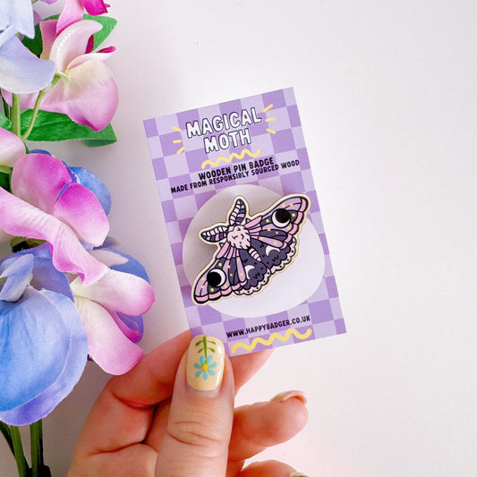 A wooden pin badge of a purple and pink moth.