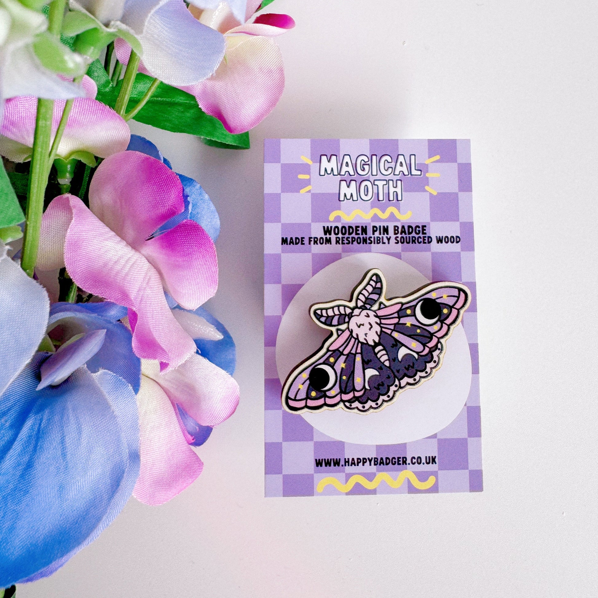 A wooden pin badge of a purple and pink moth.