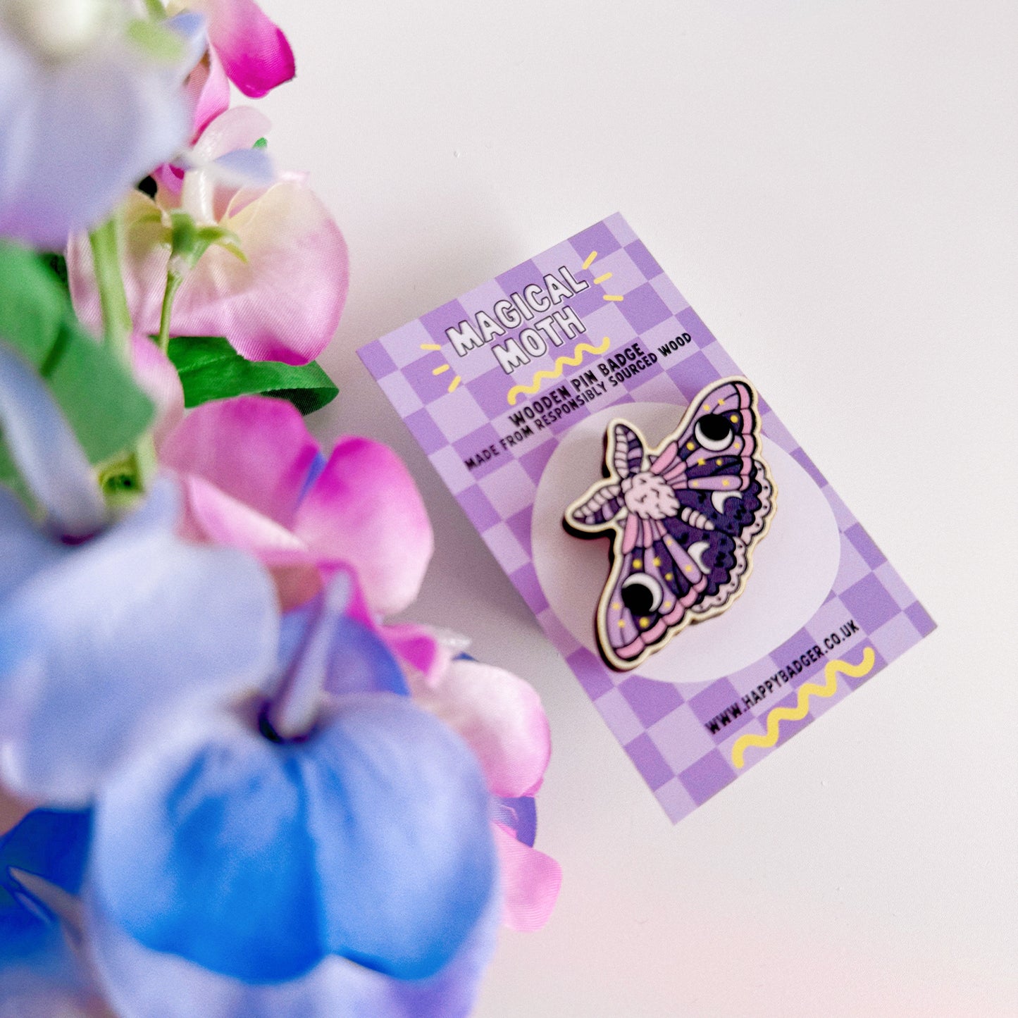 A wooden pin badge of a purple and pink moth.