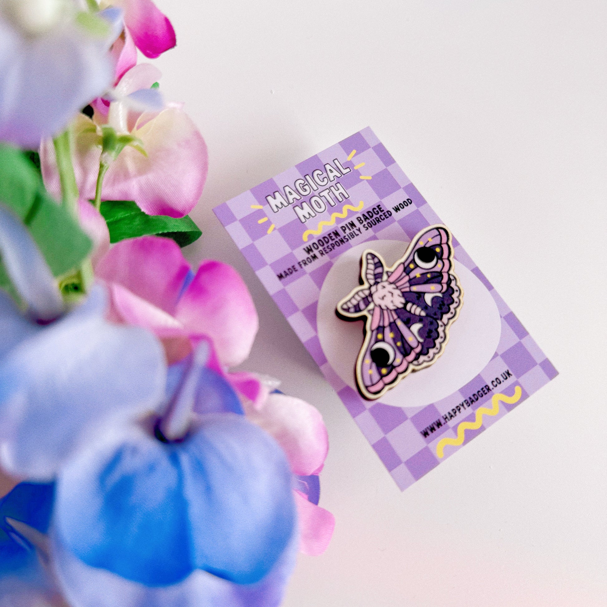 A wooden pin badge of a purple and pink moth.