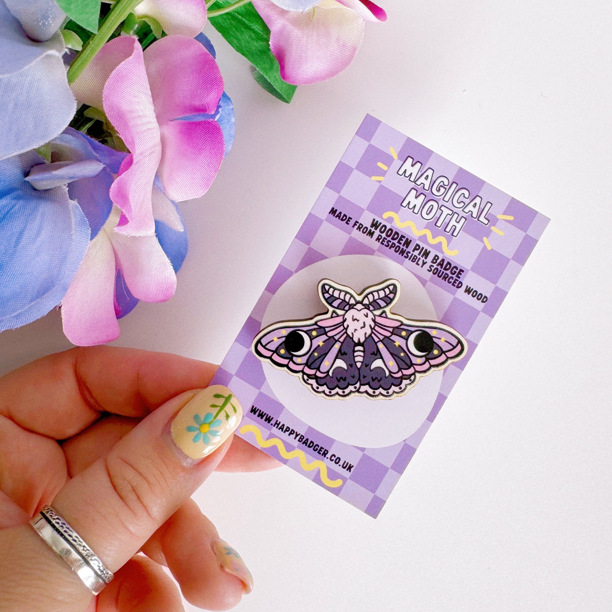 A wooden pin badge of a purple and pink moth.