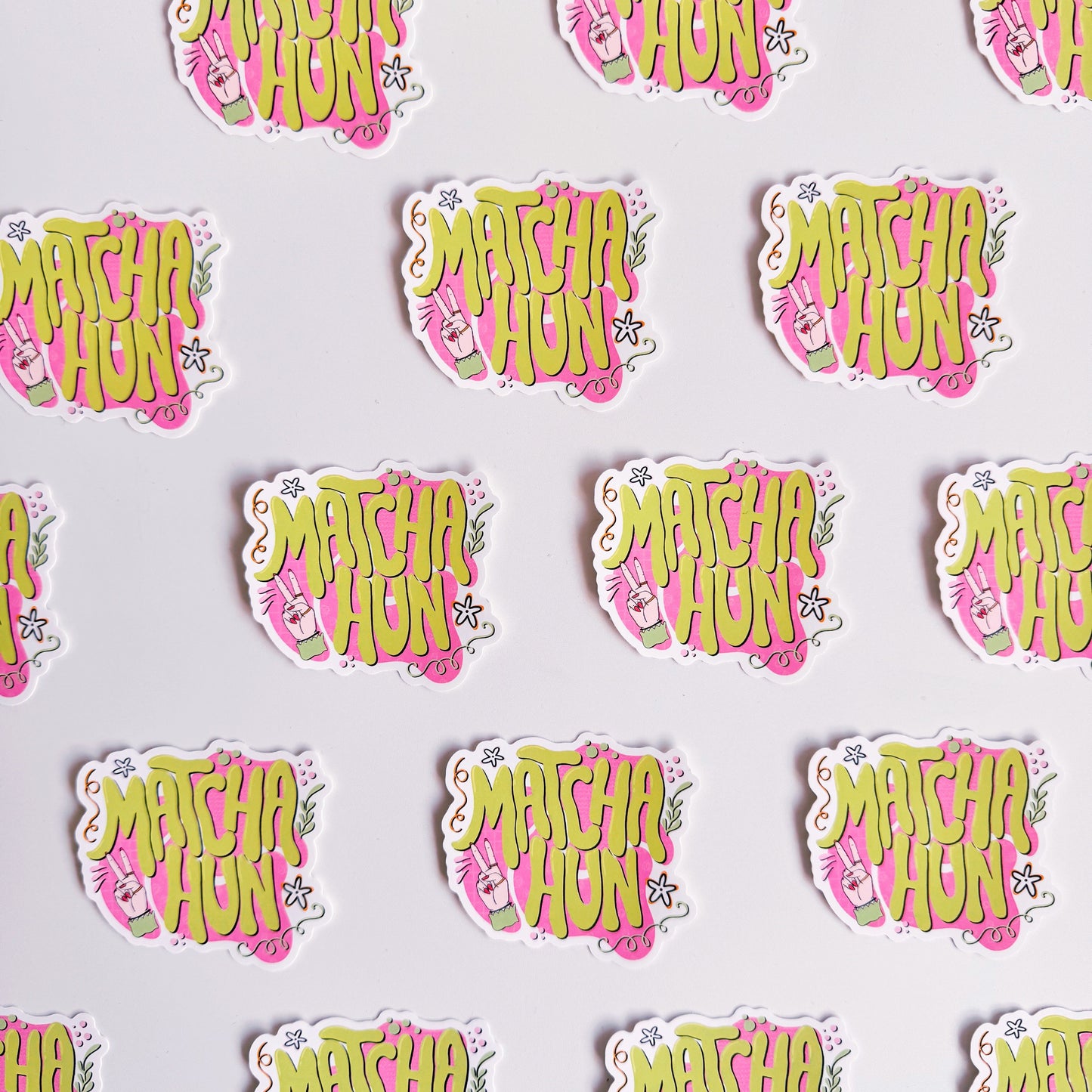 Several vinyl stickers on a white background. The vinyl sticker is pink and green and says the words 'Matcha Hun' in fun bubble writing.