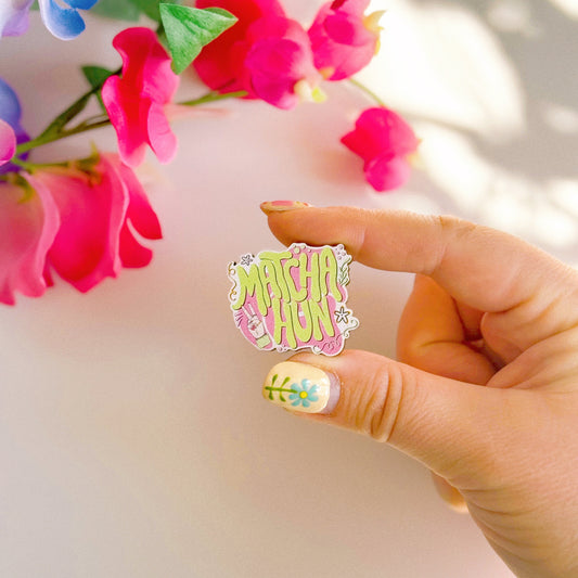 An eco friendly wooden pin badge, with a pink and green design that says 'matcha hun'.
