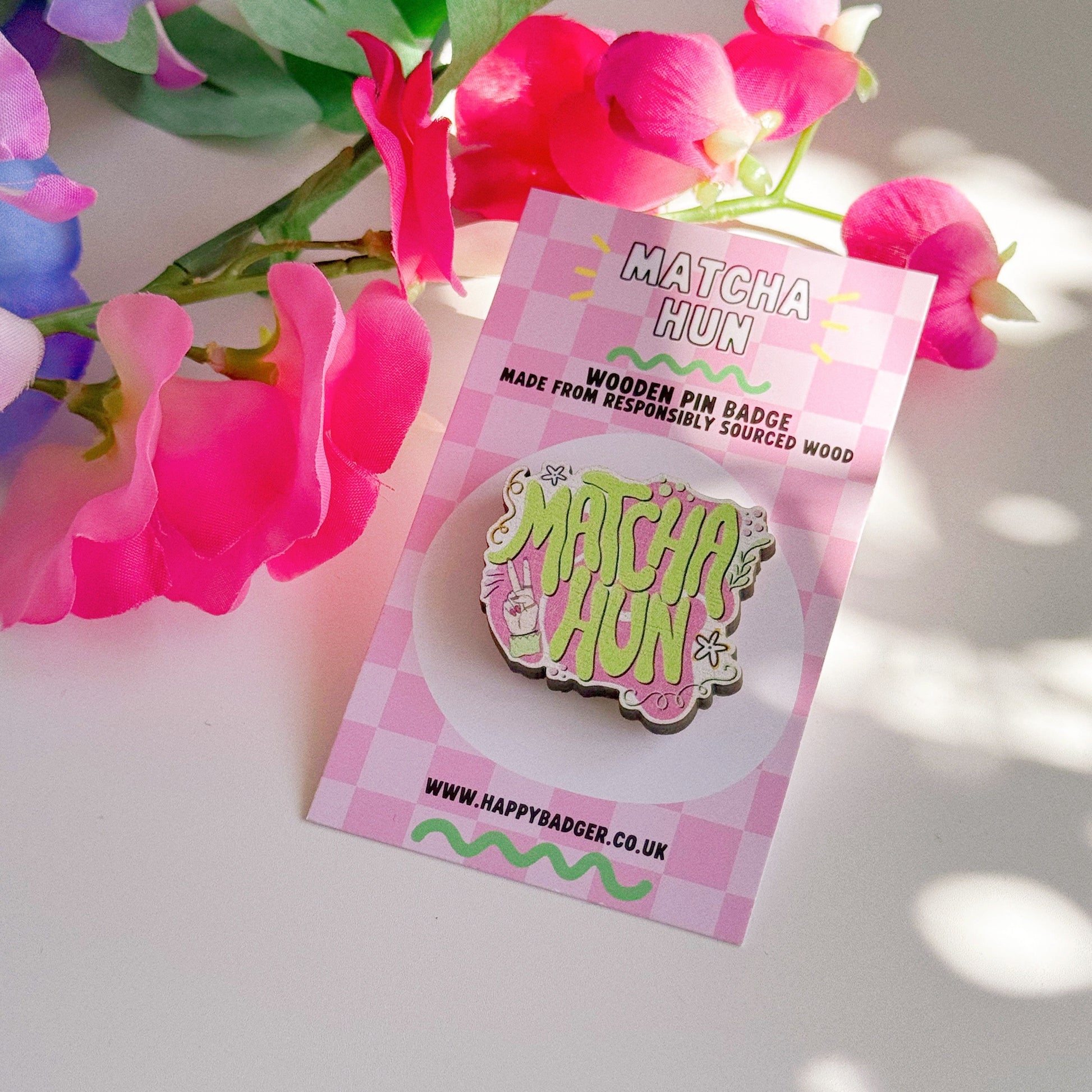 An eco friendly wooden pin badge, with a pink and green design that says 'matcha hun'.