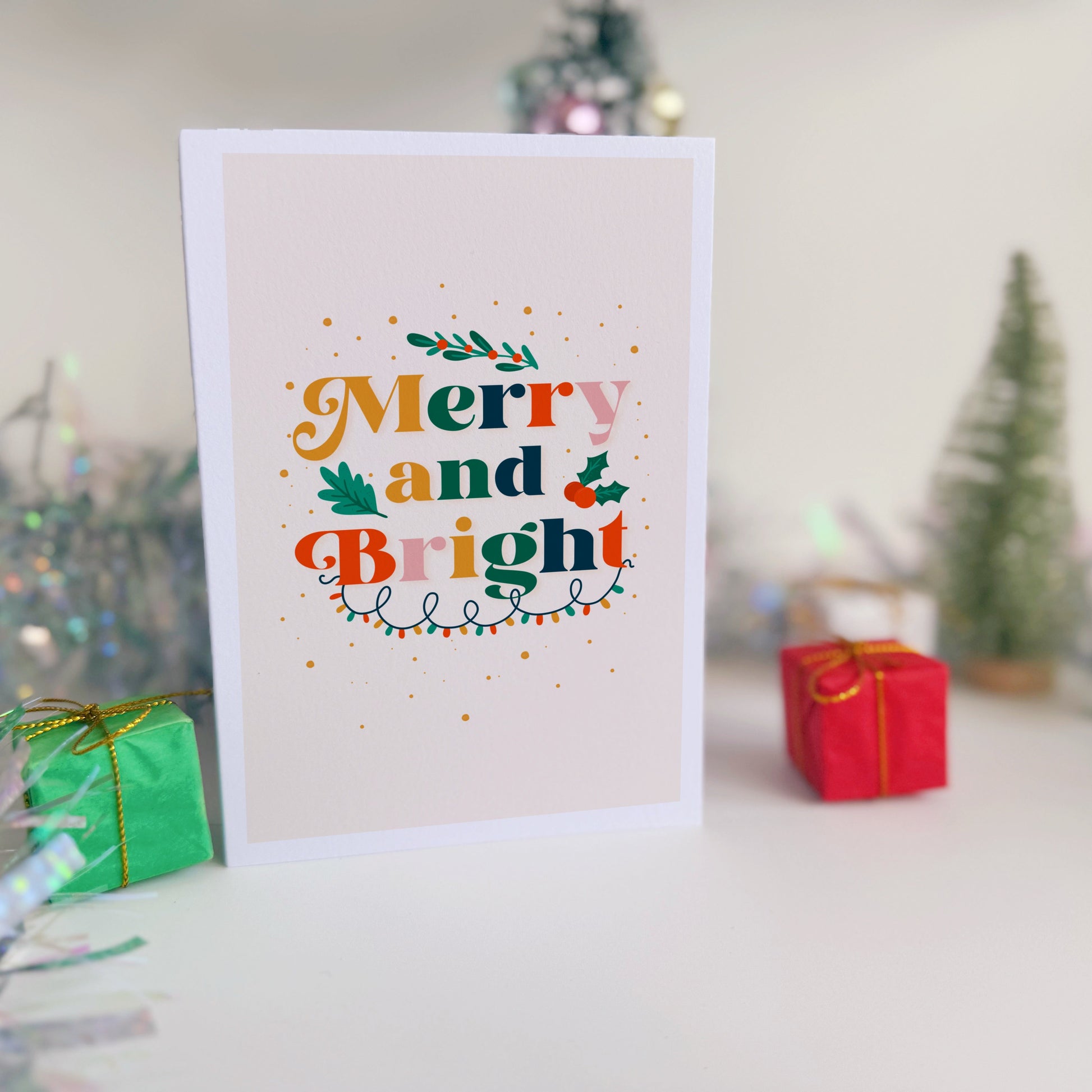 Christmas card with 'Merry and Bright' text in a festive setting with small trees and presents.