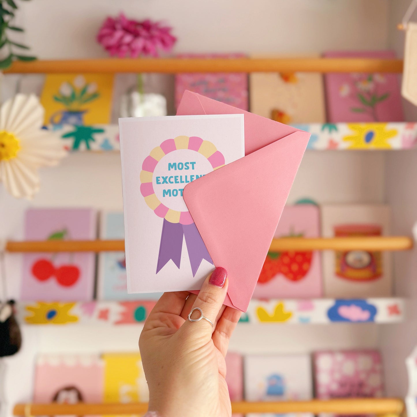 A card with a 'Most Excellent Mother' rosette in pink, yellow and purple.