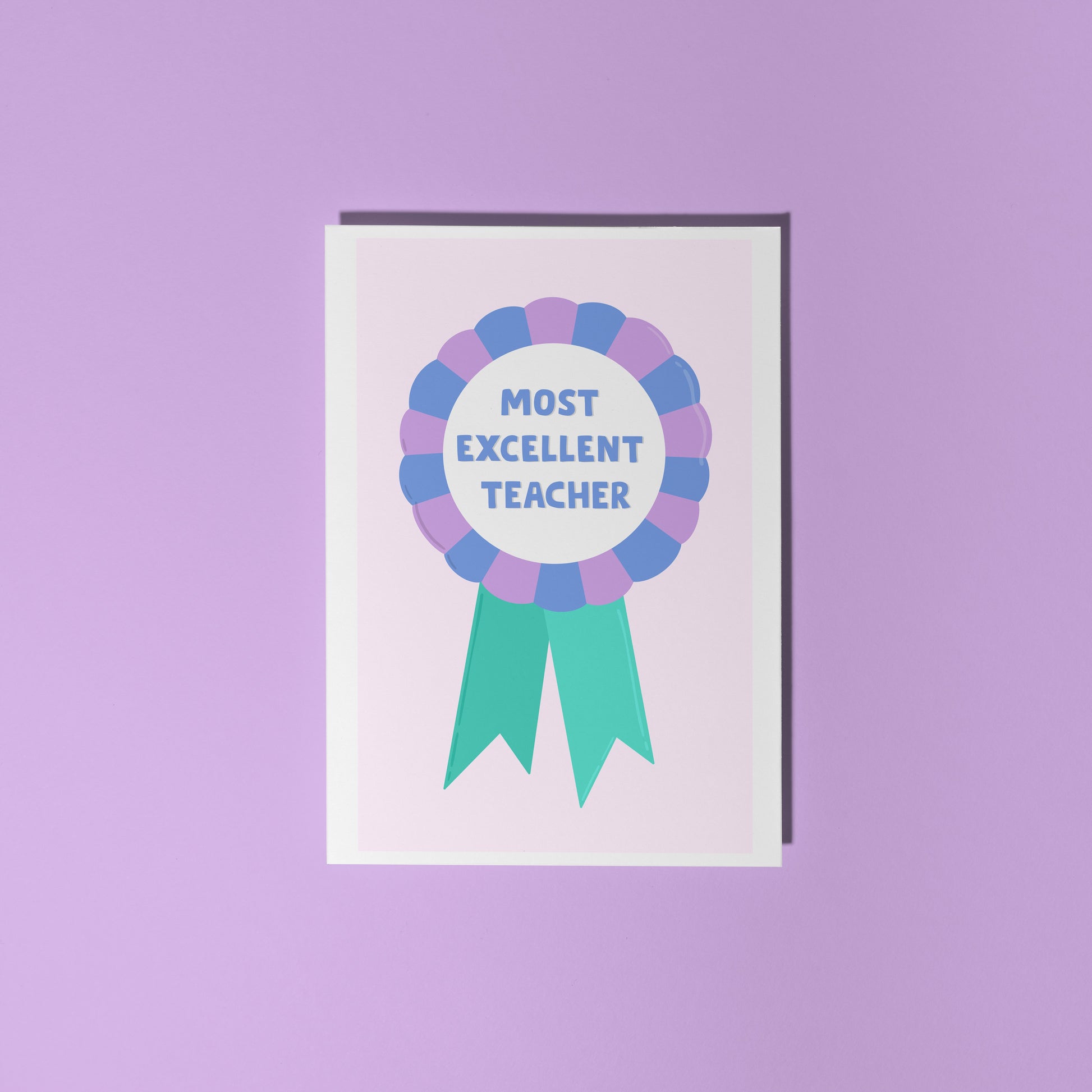 A greetings card with a rosette with text saying most excellent teacher. The colour combo is green blue and purple.