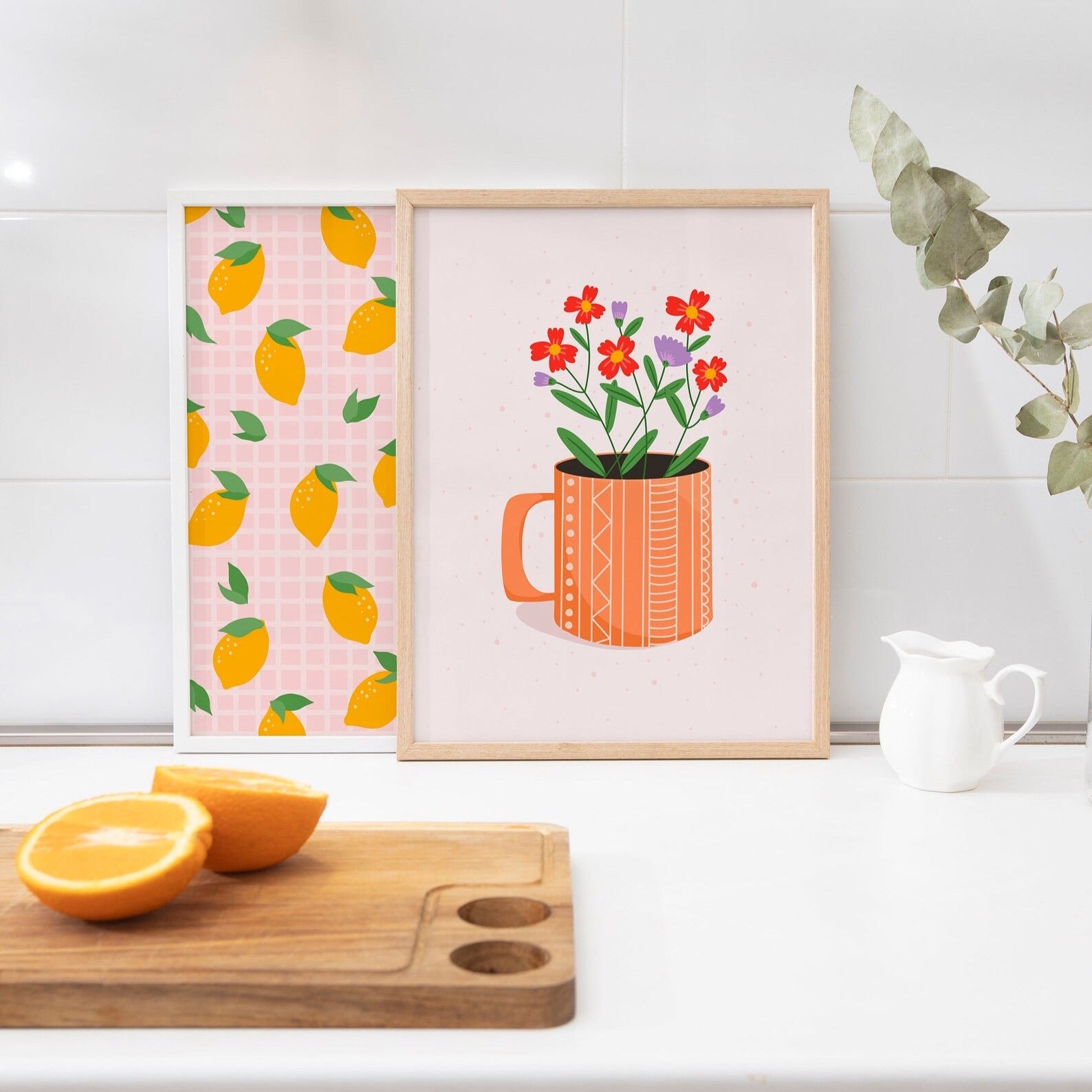 An illustration print, of an orange mug with red and purple flowers in on a pale pink to off-white background. Shown next to a lemon pattern print.