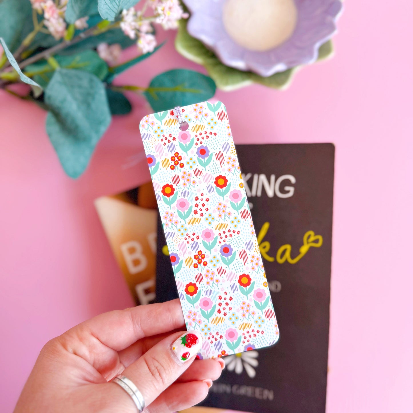 A multi coloured floral bookmark, with a coordinating lilac purple tassel. The pattern is on a white background and features pink, green, purple and red across the flower pattern.