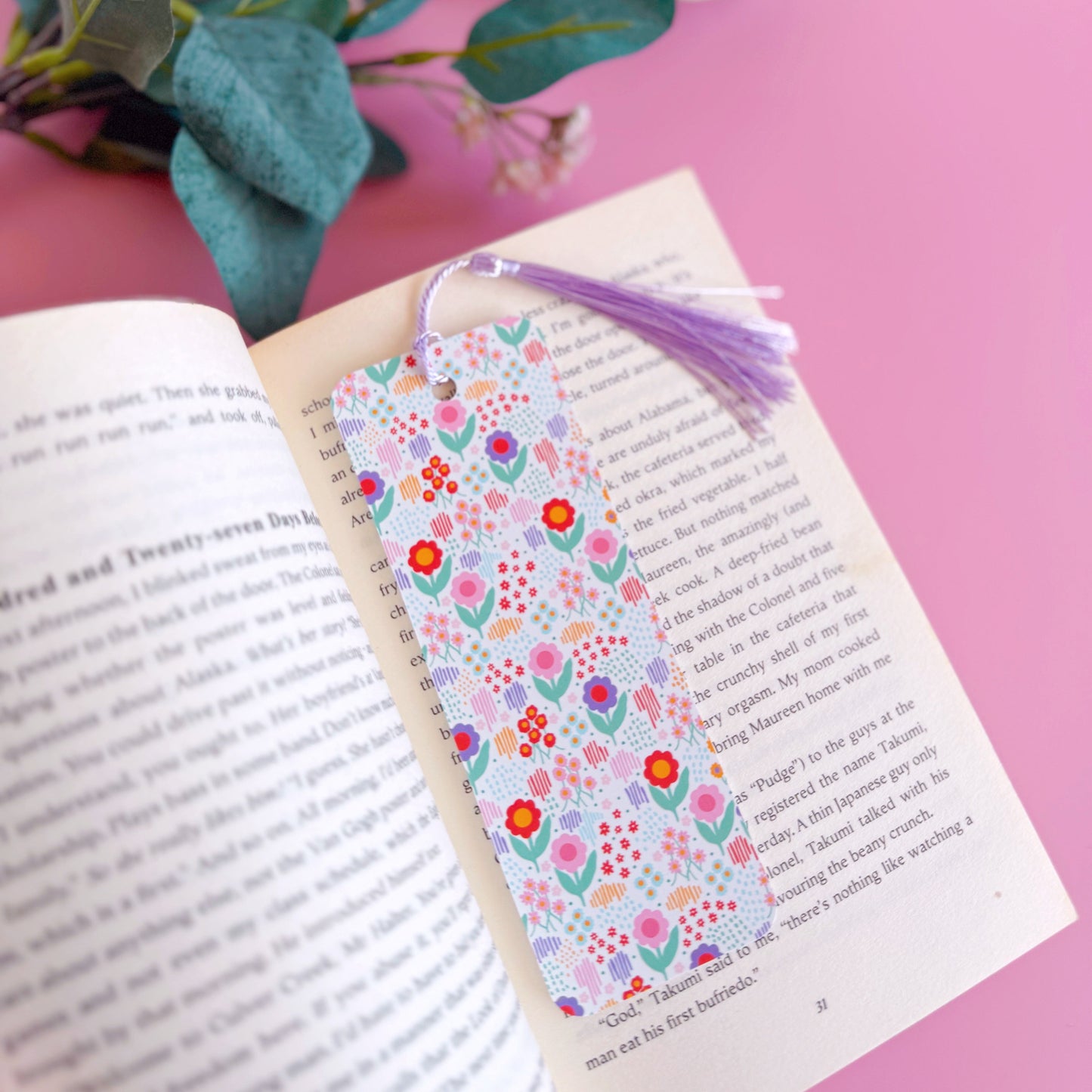 A multi coloured floral bookmark, with a coordinating lilac purple tassel. The pattern is on a white background and features pink, green, purple and red across the flower pattern.