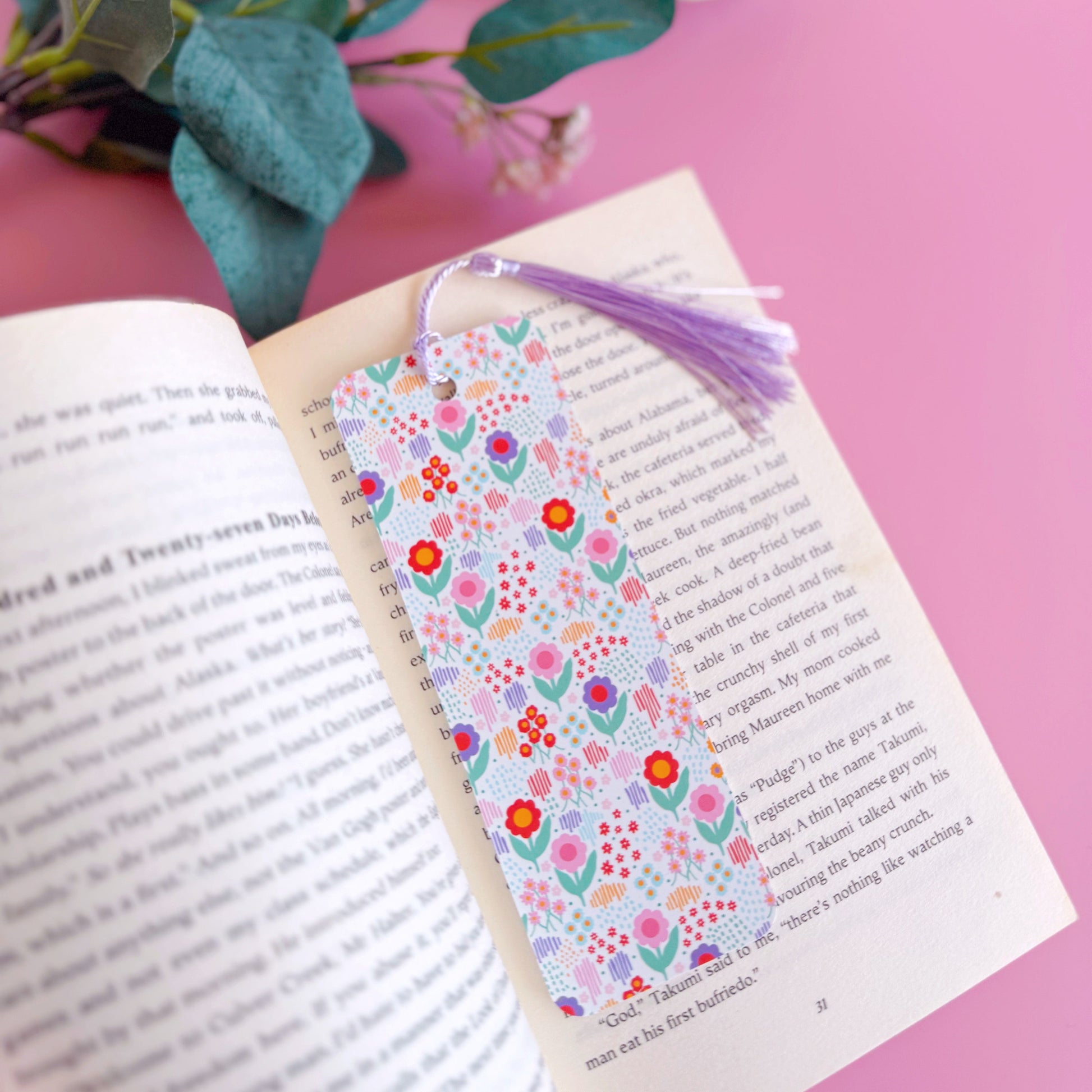 A multi coloured floral bookmark, with a coordinating lilac purple tassel. The pattern is on a white background and features pink, green, purple and red across the flower pattern.