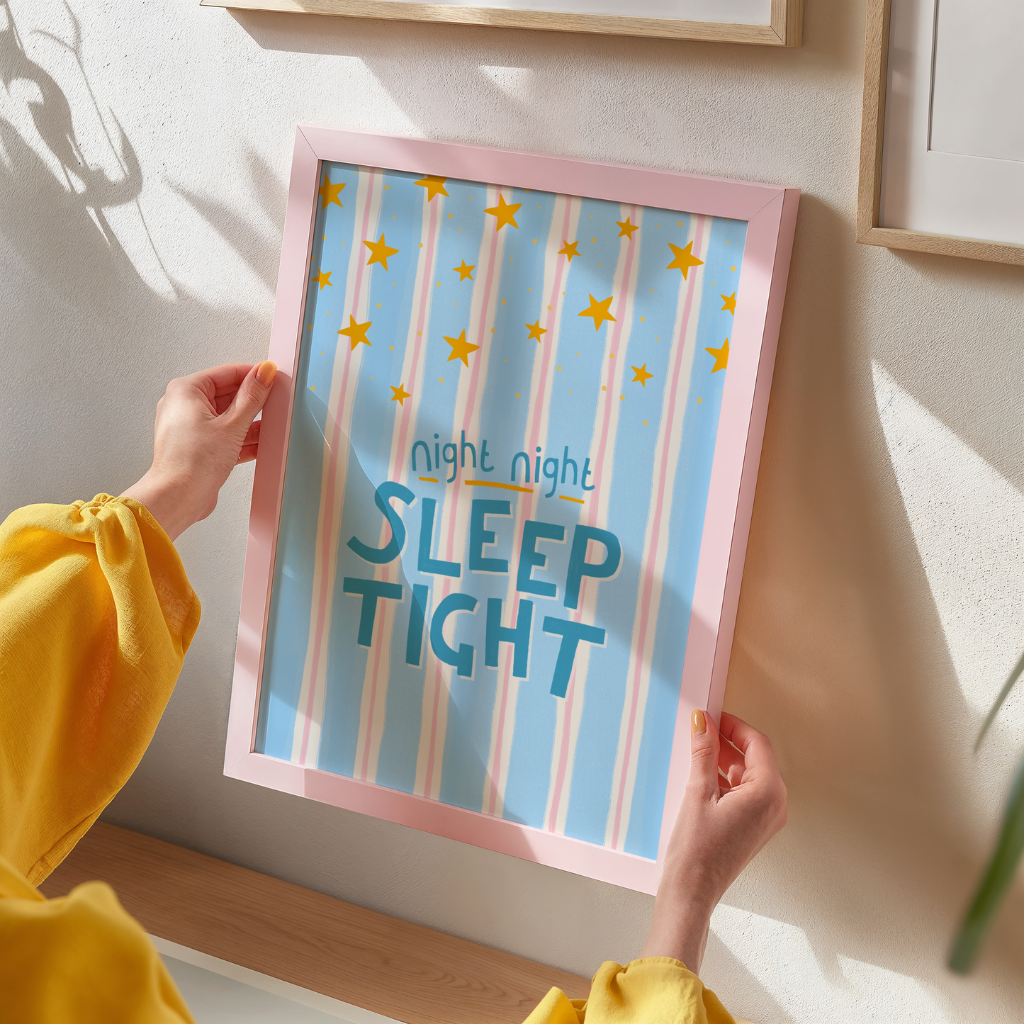 Person holding a framed print with 'night night SLEEP TIGHT' text against a light wall.