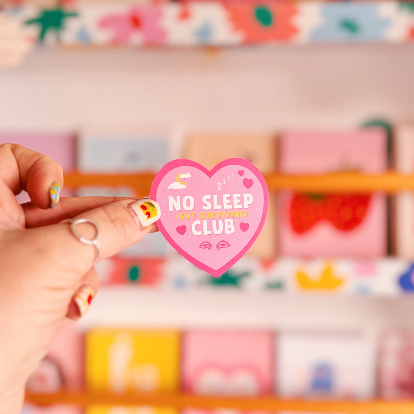 A pink heart-shaped sticker with a 'No Sleep Club' quote and little illustrations relating to sleep and tiredness.