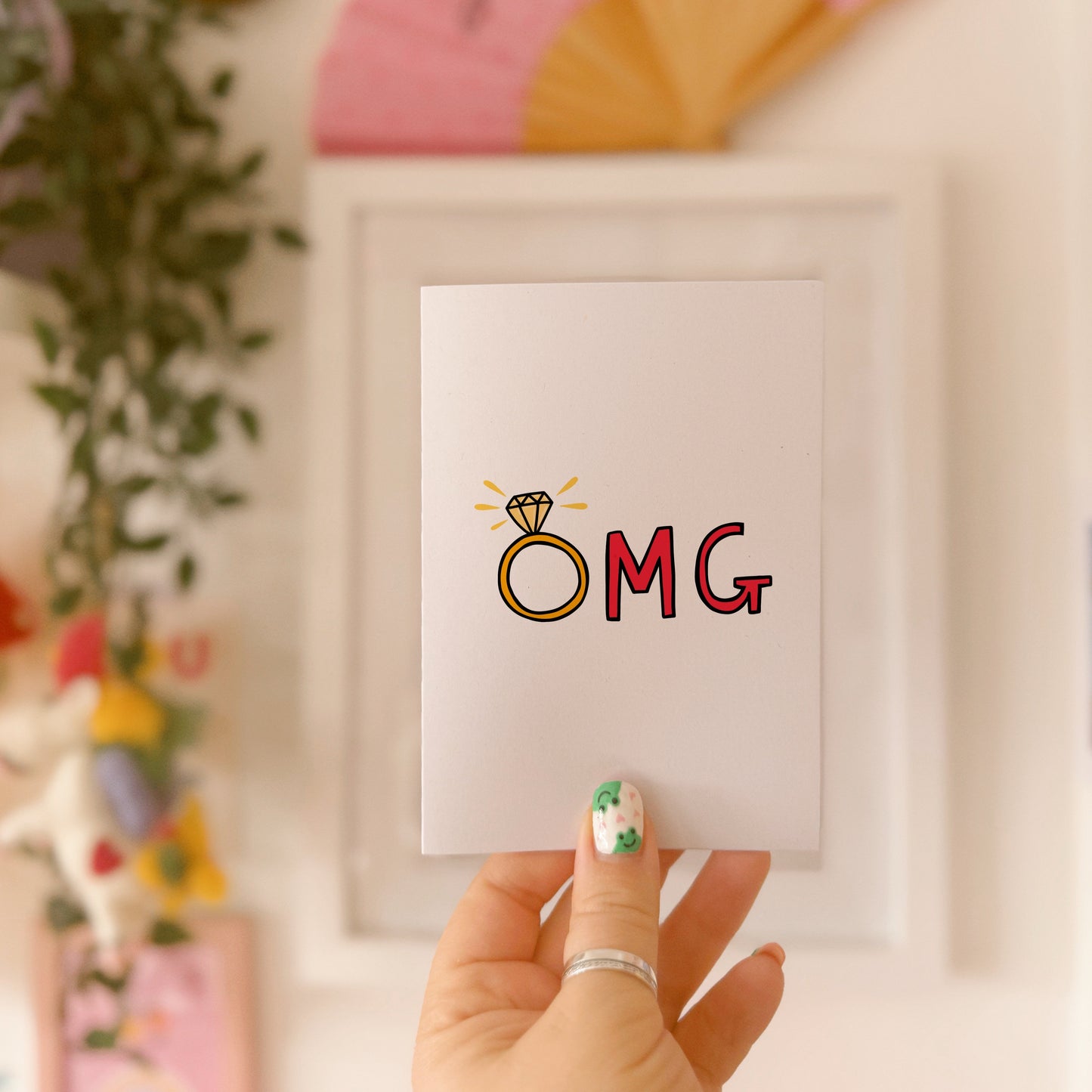 A greetings card that says OMG in hand drawn lettering, with the O as an engagement ring.