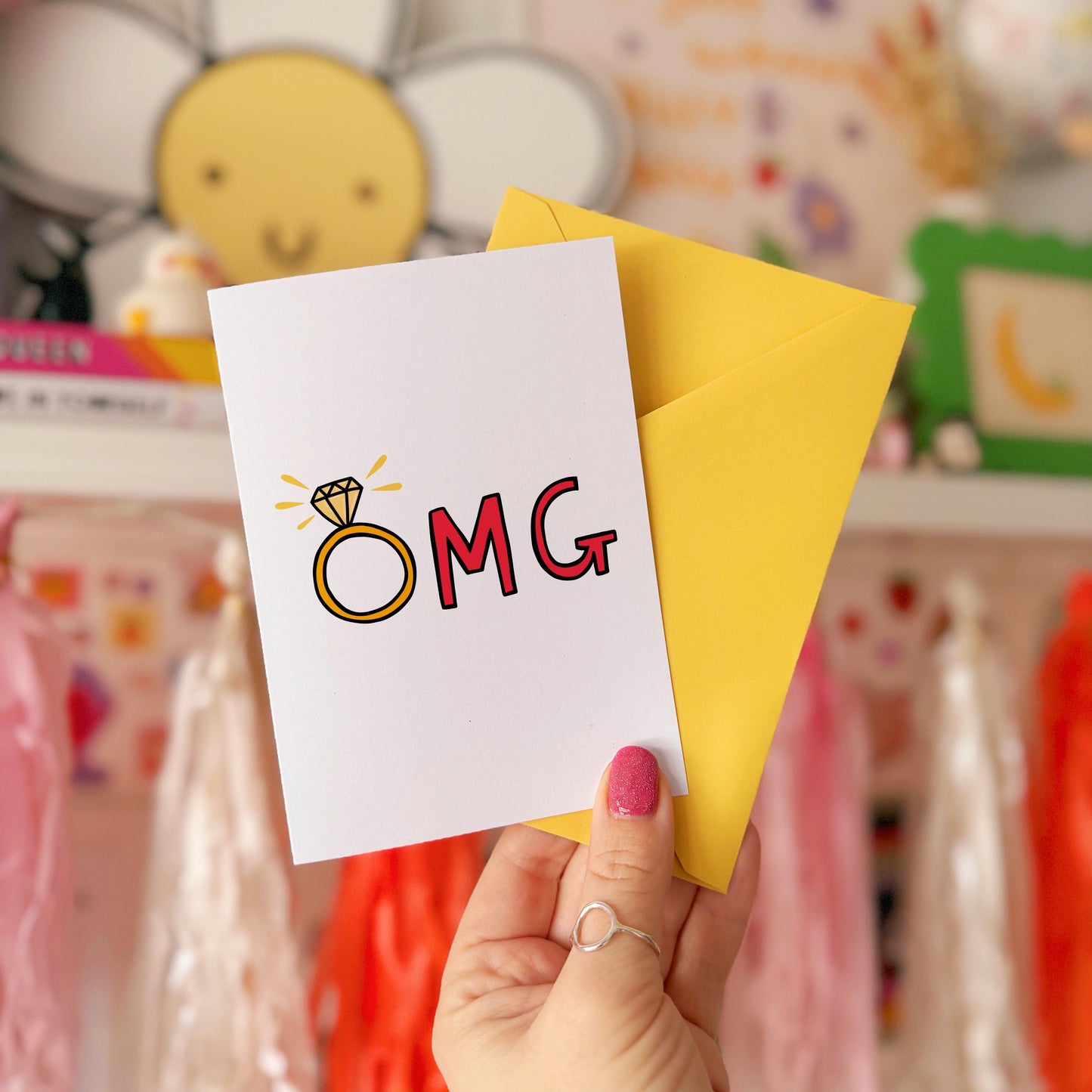 A greetings card that says OMG in hand drawn lettering, with the O as an engagement ring.