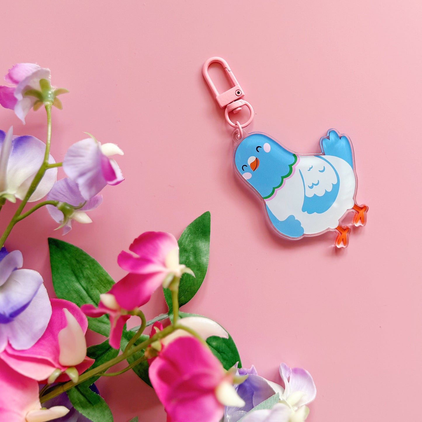 Bird-shaped keychain with a pink clip on a pink background with flowers