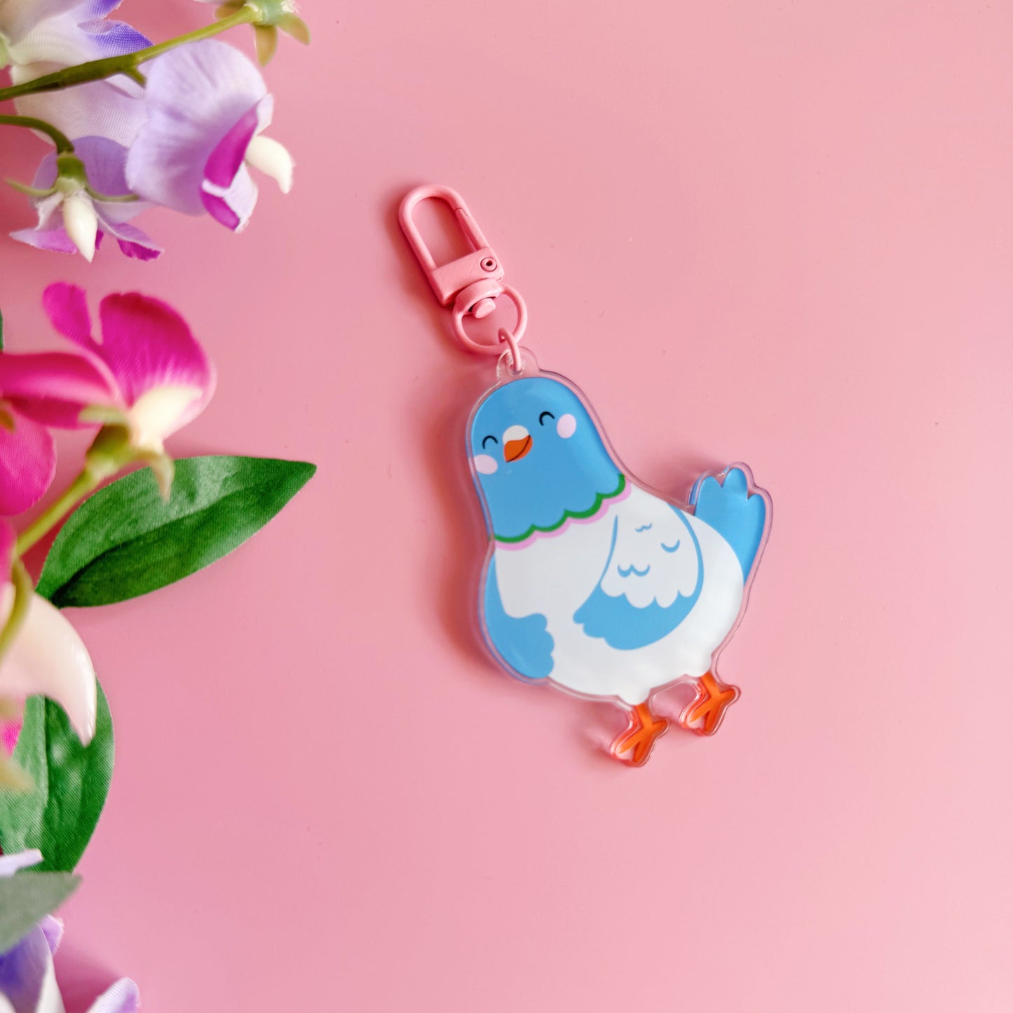Blue cartoon pigeon keychain on a pink background with flowers