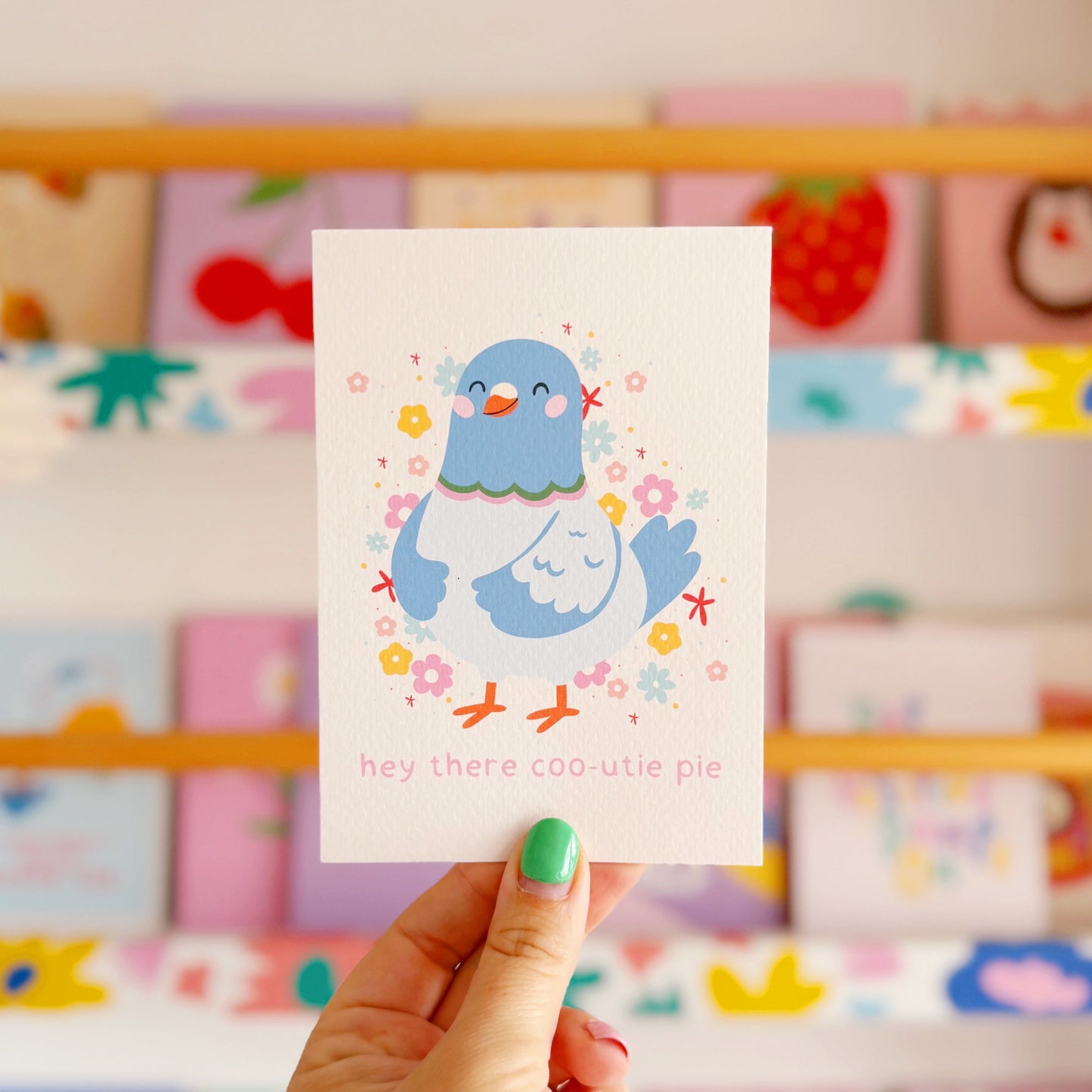 Hand holding a card with a blue cartoon character in front of a colorful shelf.