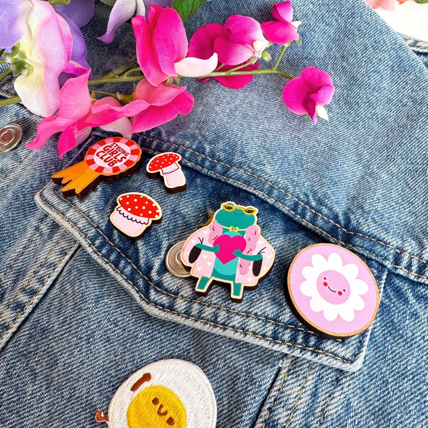 A collection of wooden pin badges shown on a denim jacket.