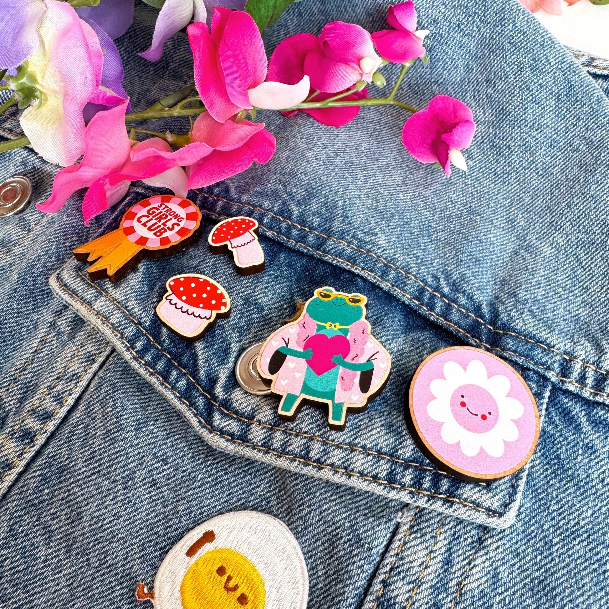 A collection of wooden pin badges shown on a denim jacket.