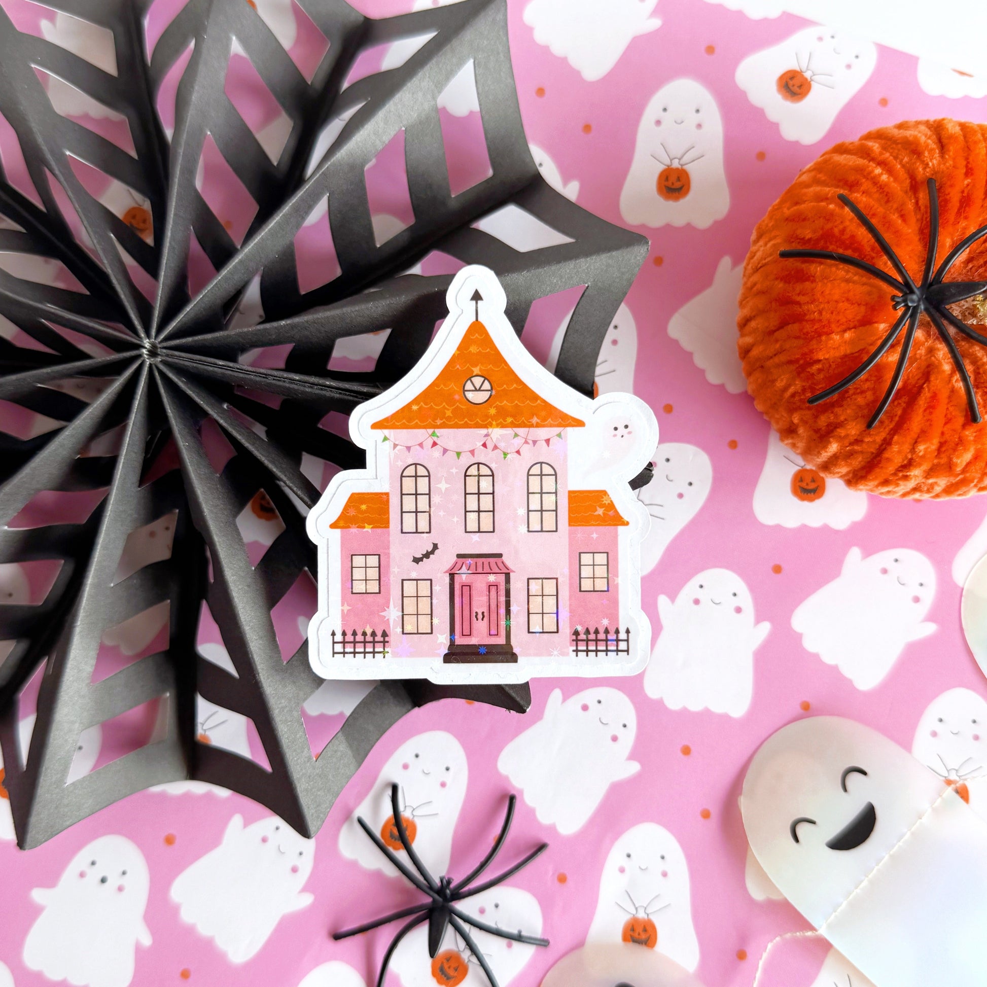 A holographic sticker, a pink and orange haunted house with a glittery finish. The sticker has an easy peel lip.