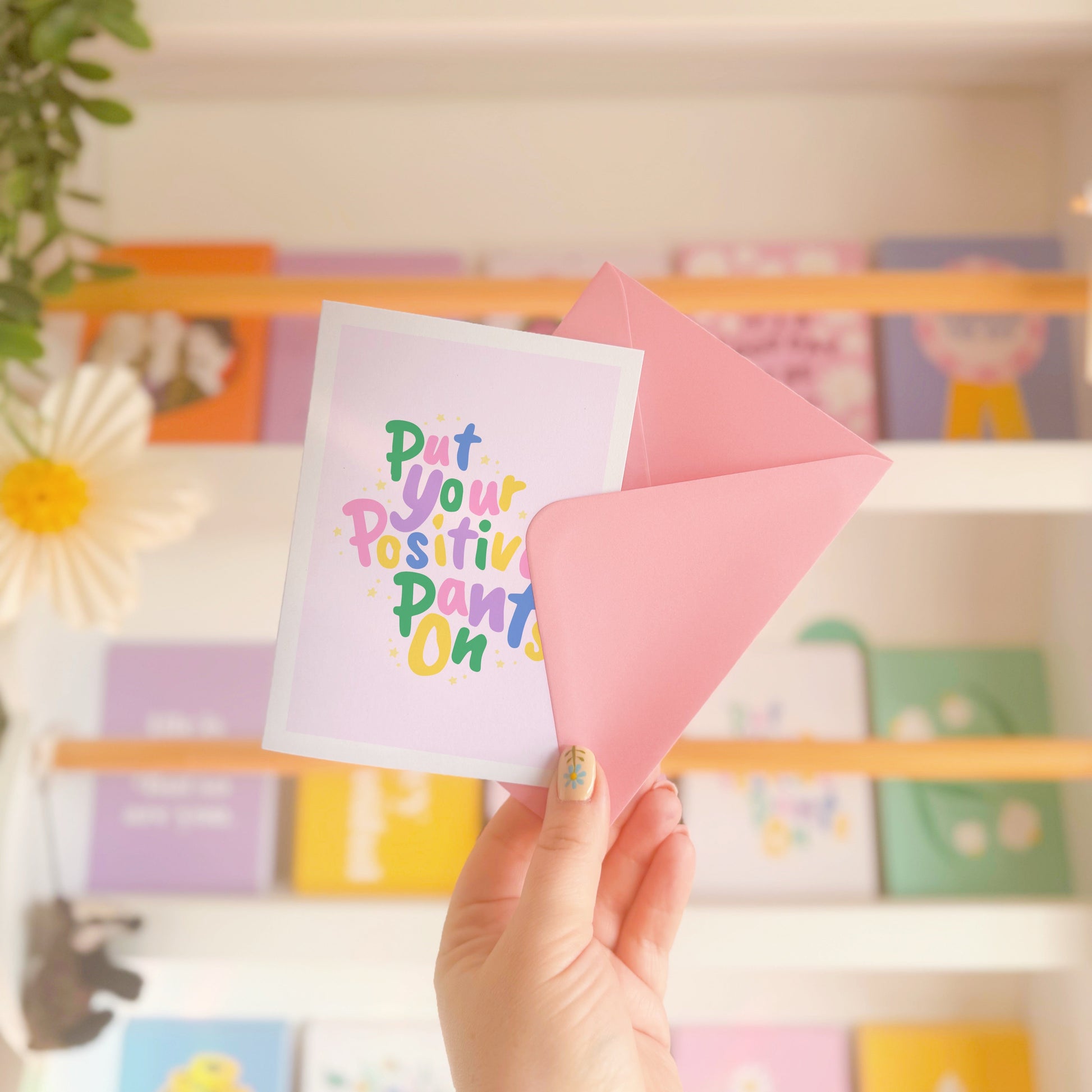 A colourful card with hand lettered text, saying 'put your positive pants on' on a light pink background.