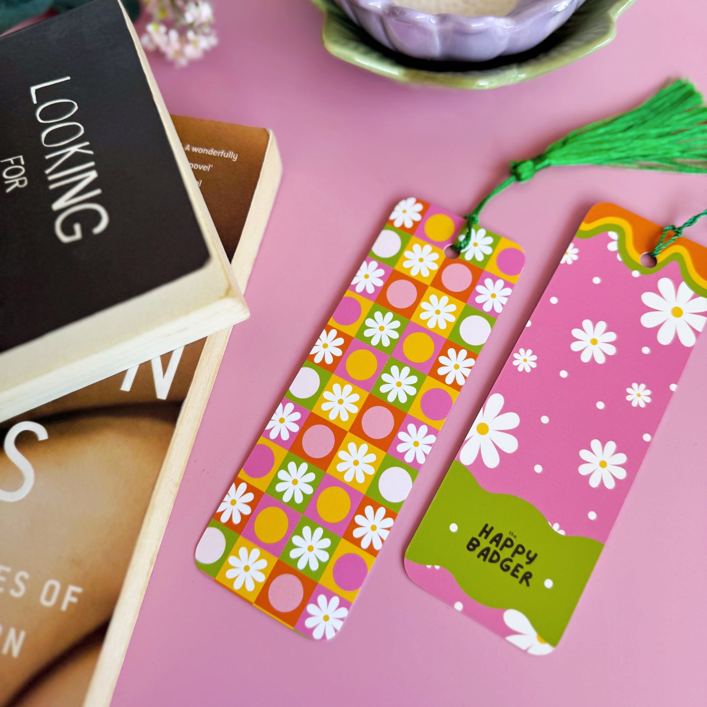 A brightly coloured retro look bookmark, featuring a checkerboard pattern with daisies and circles, in pink, green, yellow and orange. The bookmark has a coordinating green tassel.