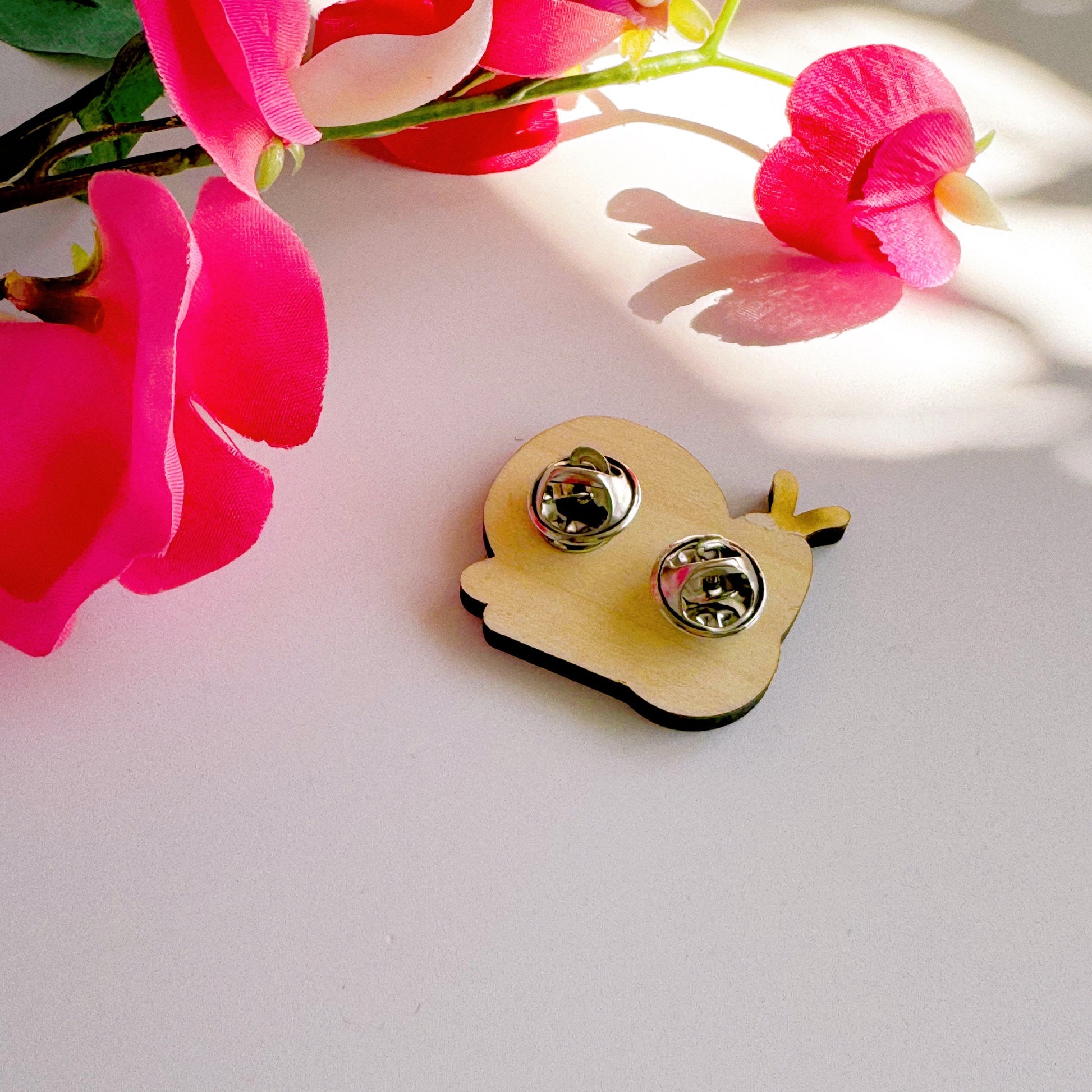 The back of a wooden pin badge with two metal clasp fastenings.