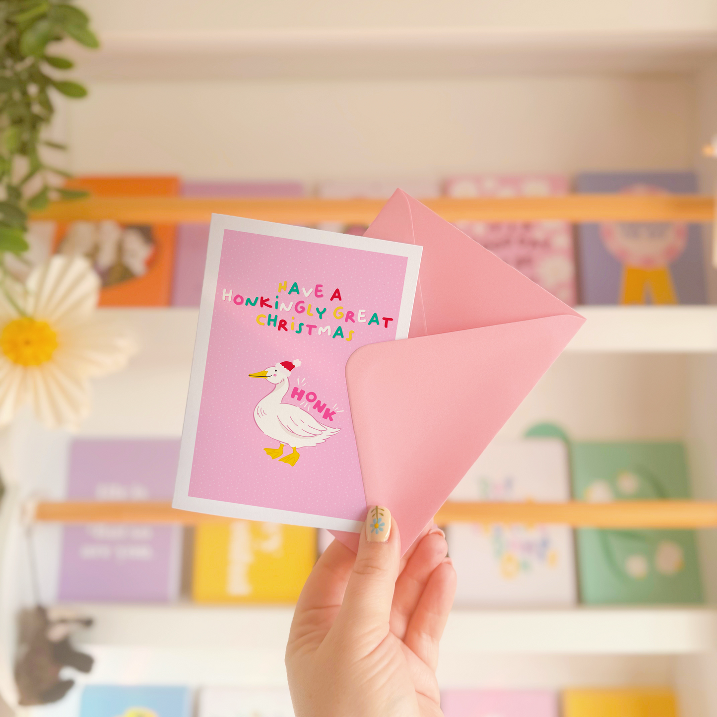 A pink greetings card, with an illustration of a goose wearing a christmas hat. Above the goose, are the words 'have a honkingly great Christmas'. Next to the goose is also the word 'HONK', as if to show him honking.