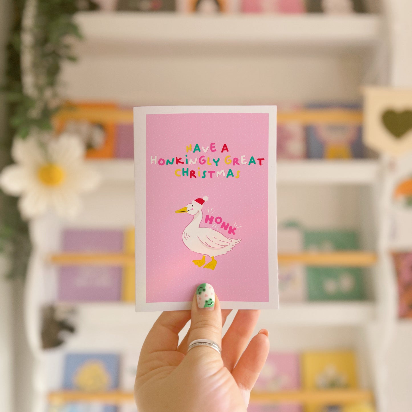 A pink greetings card, with an illustration of a goose wearing a christmas hat. Above the goose, are the words 'have a honkingly great Christmas'. Next to the goose is also the word 'HONK', as if to show him honking.