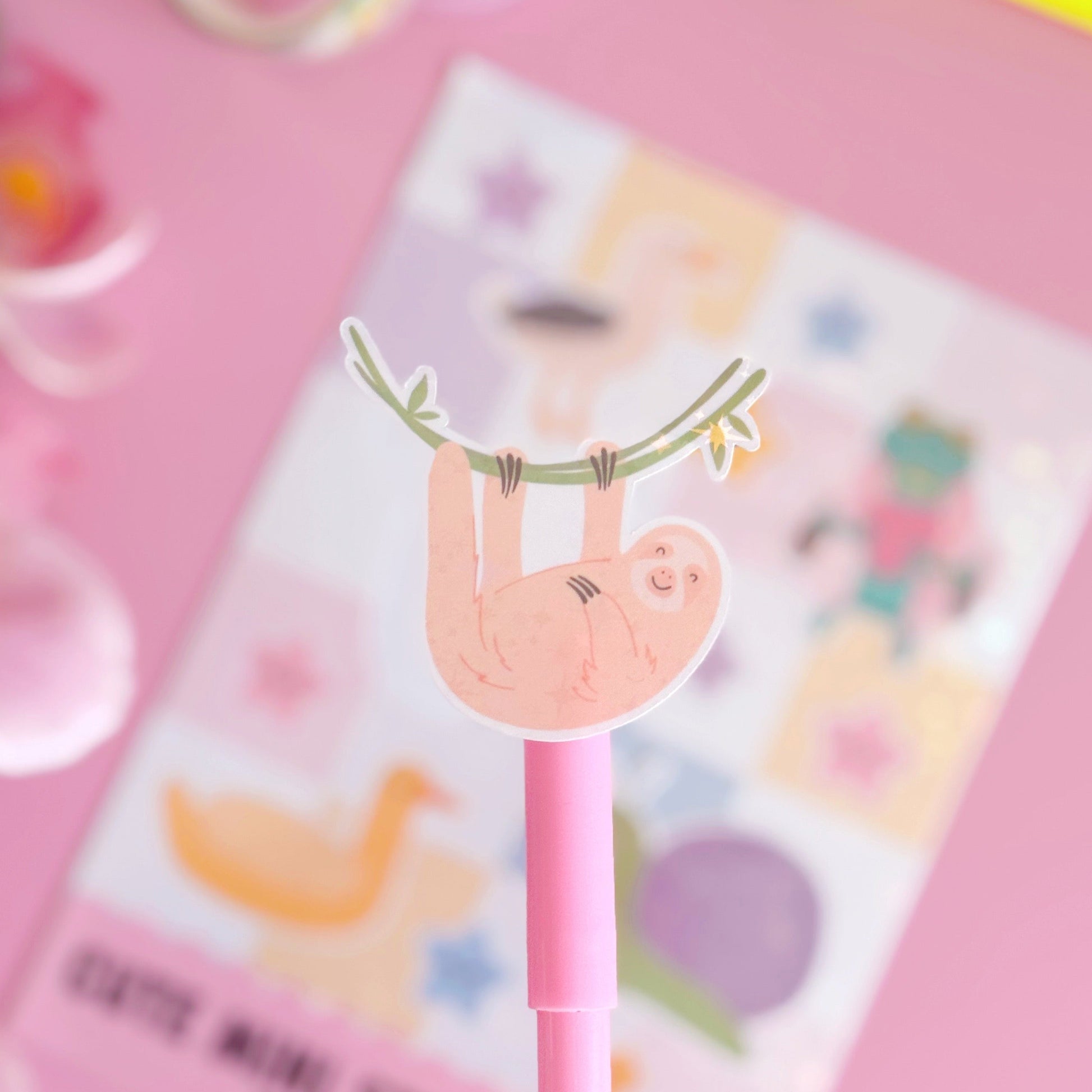 A sticker from the mini sticker pals sticker sheet. This is a sloth hanging from a branch, coated with a holographic laminate with little starbursts on.