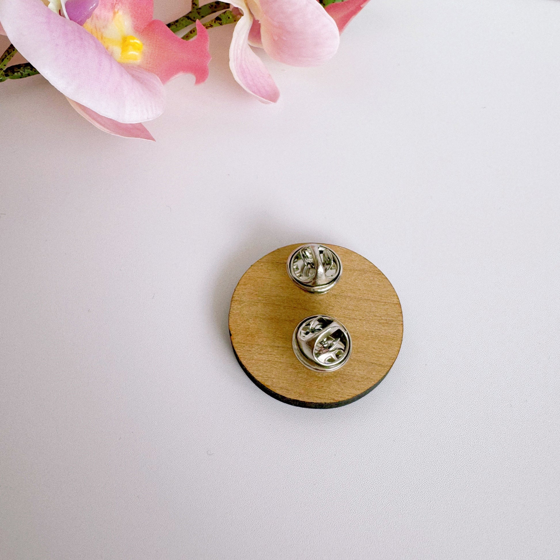 The back of the smiling daisy pin badge which has two metal clasp fastenings.