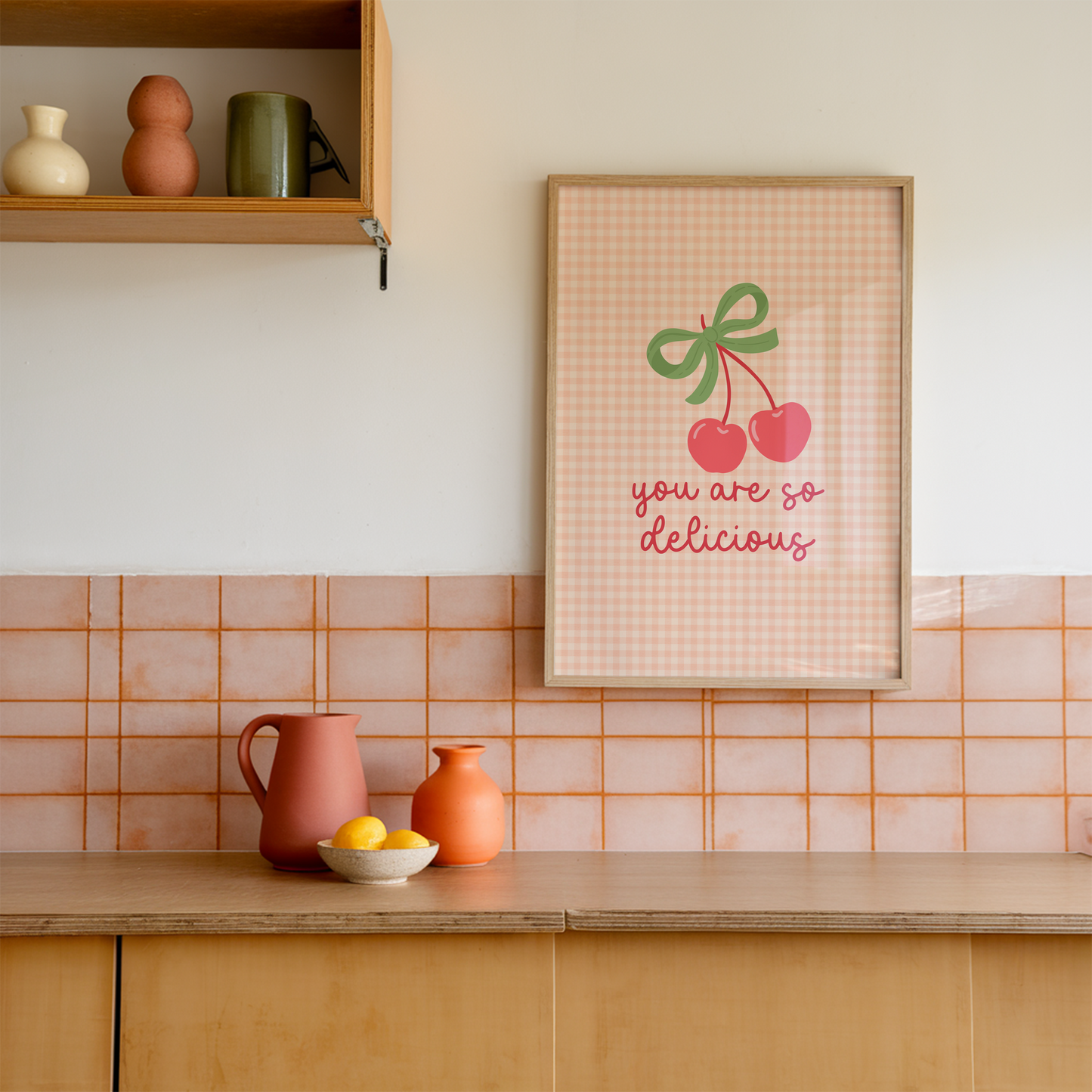 An orange gingham background print, with an illustration of red cherries tied together with a green bow, and the quote saying 'you are so delicious' below.