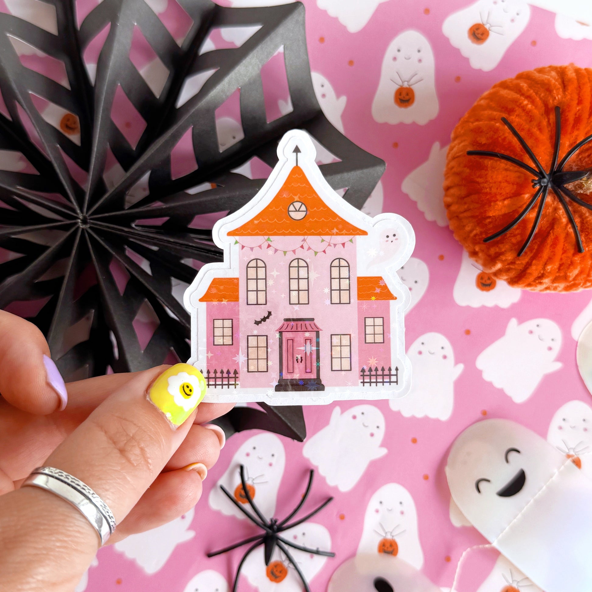 A holographic sticker, a pink and orange haunted house with a glittery finish. The sticker has an easy peel lip.