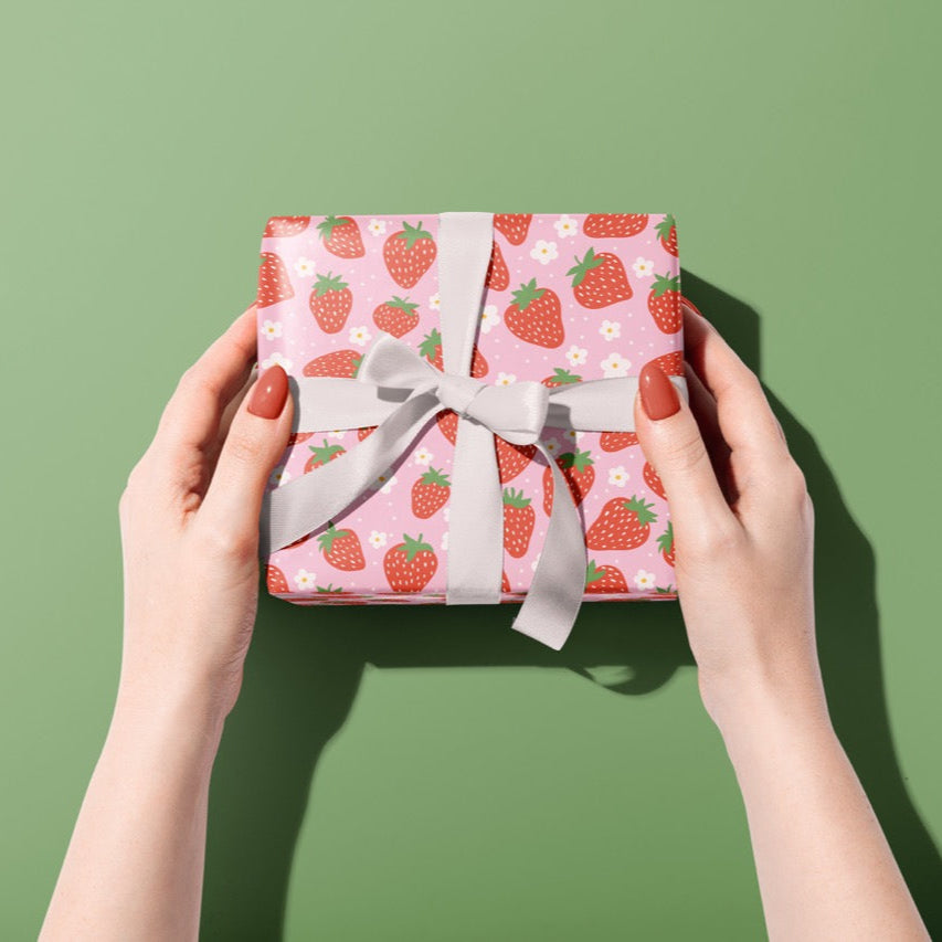 A gift wrapped present, wrapped up in bright pink and red strawberry print gift wrap from The Happy Badger.